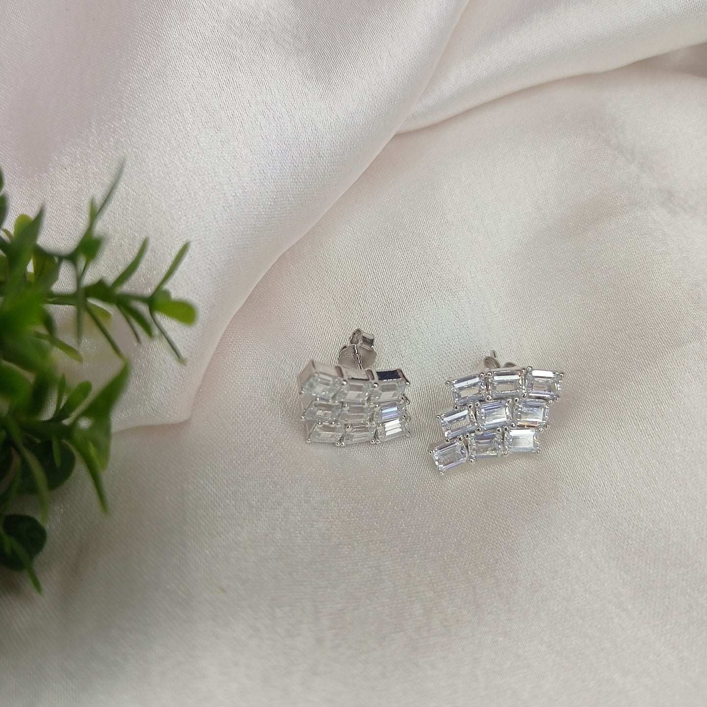 Close-up of a hand holding a pair of elegant silver-tone ear climbers adorned with a row of sparkling baguette-cut stones arranged in a curved, geometric pattern. These statement earrings add a modern yet sophisticated touch to any look