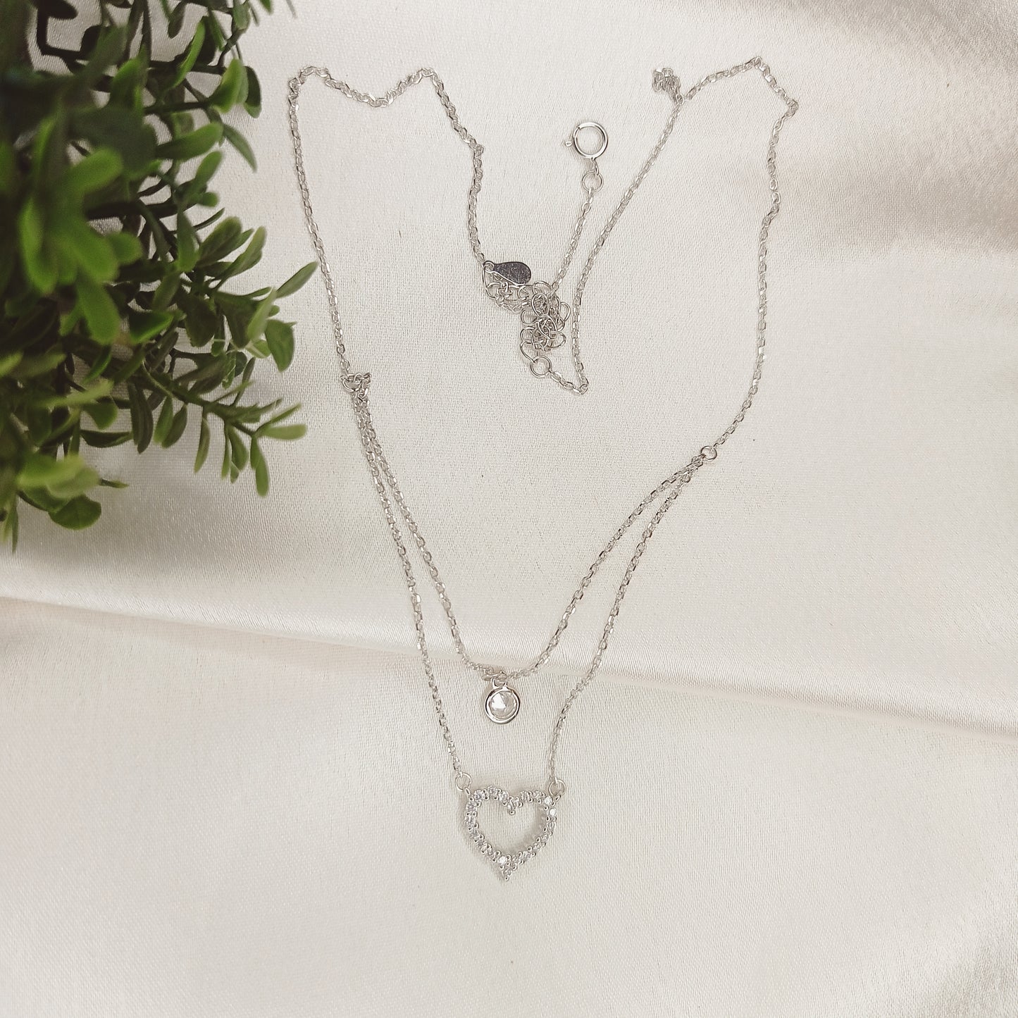 Elegant layered silver necklace featuring a delicate solitaire pendant on the upper chain and a sparkling crystal-studded heart pendant on the lower chain, adding a touch of sophistication and charm