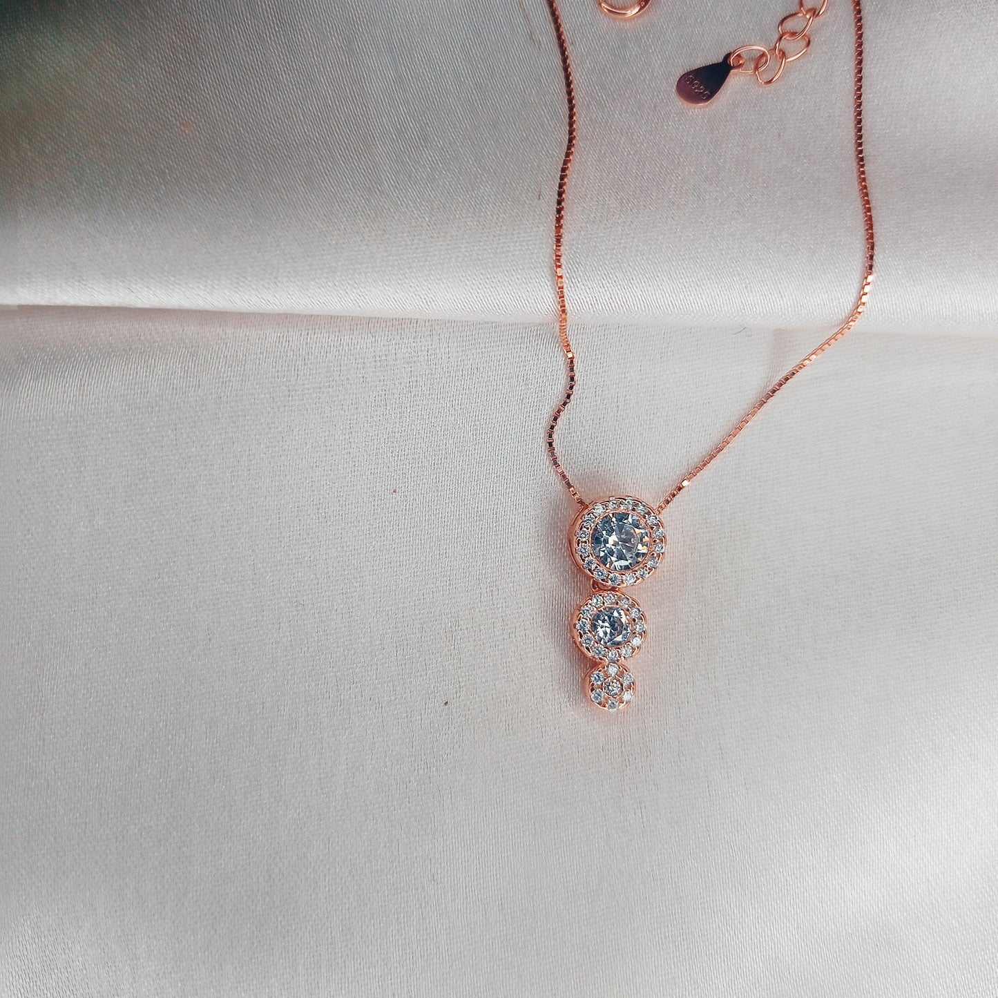 Elegant rose gold necklace featuring a three-stone drop pendant adorned with sparkling crystals, gracefully worn with a black outfit for a sophisticated look