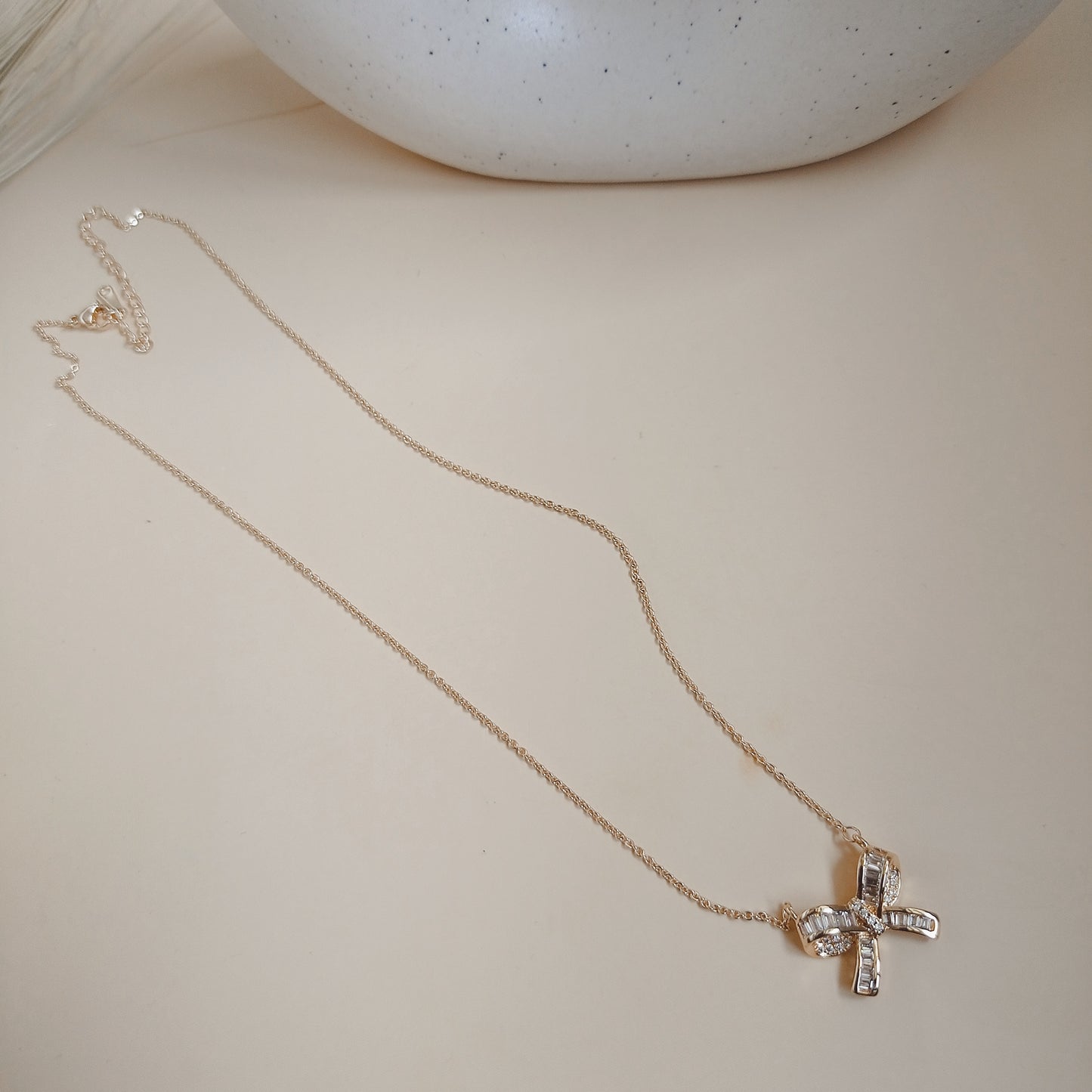 Rose gold necklace with a bow-shaped pendant featuring baguette-cut and round sparkling stones, displayed against a neutral background