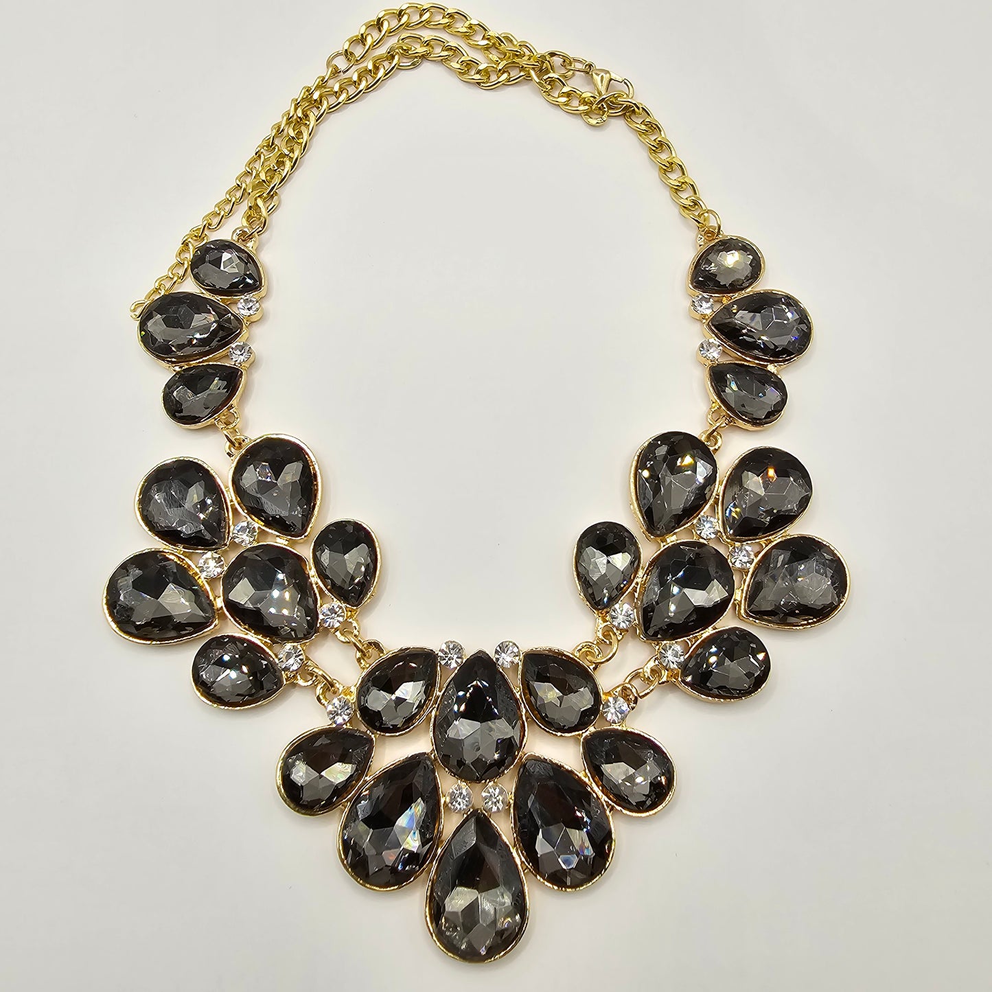 A glamorous gold-tone statement necklace adorned with faceted black teardrop crystals, elegantly arranged in a cascading floral design, displayed on a mannequin bust.