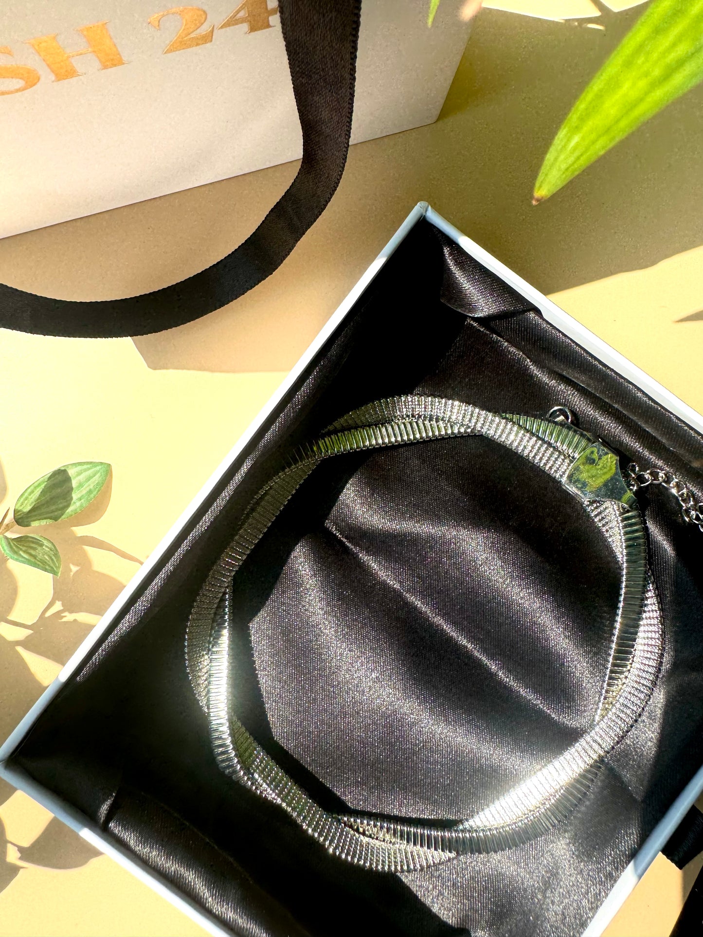 A sleek and modern silver-toned necklace with a coiled, tubular design, elegantly displayed on a white bust stand, with luxury packaging in the background