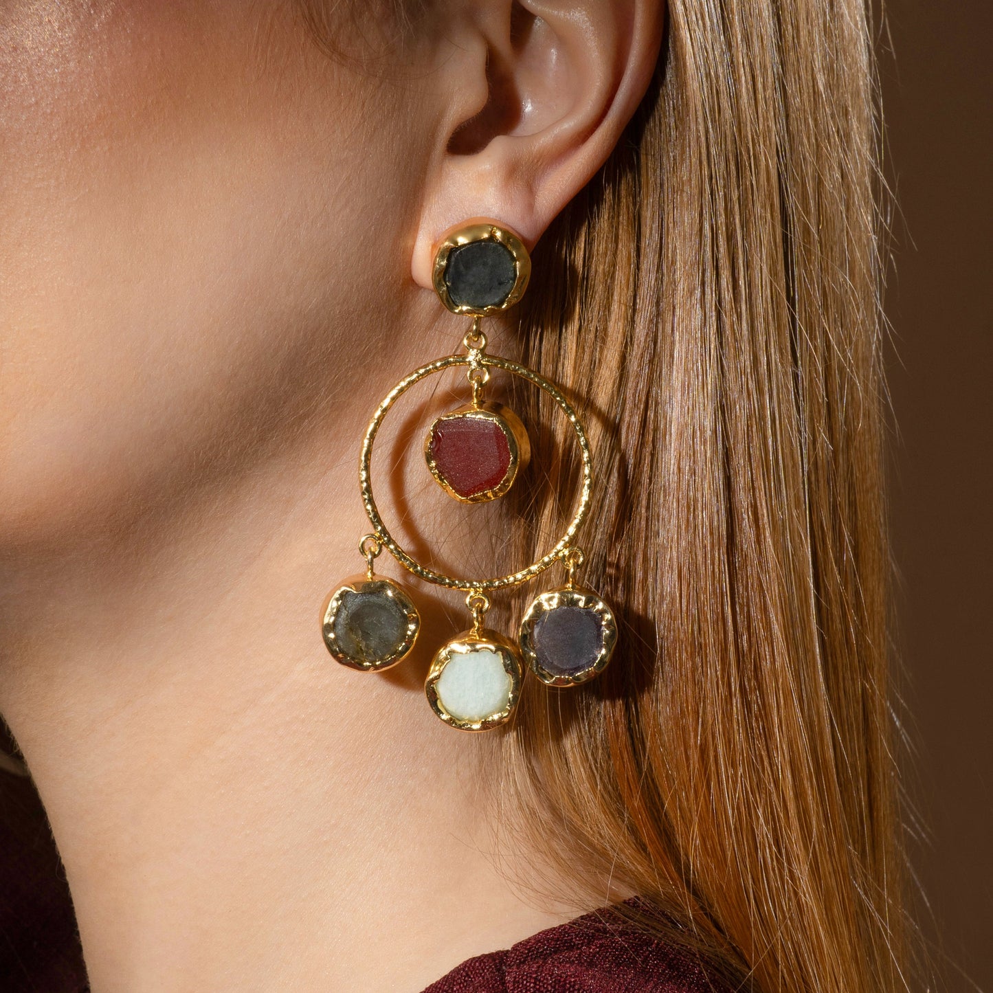 model wearing statement gold dangle earrings with raw, multicolored stone accents set in textured gold frames for a bold and artistic jewelry look