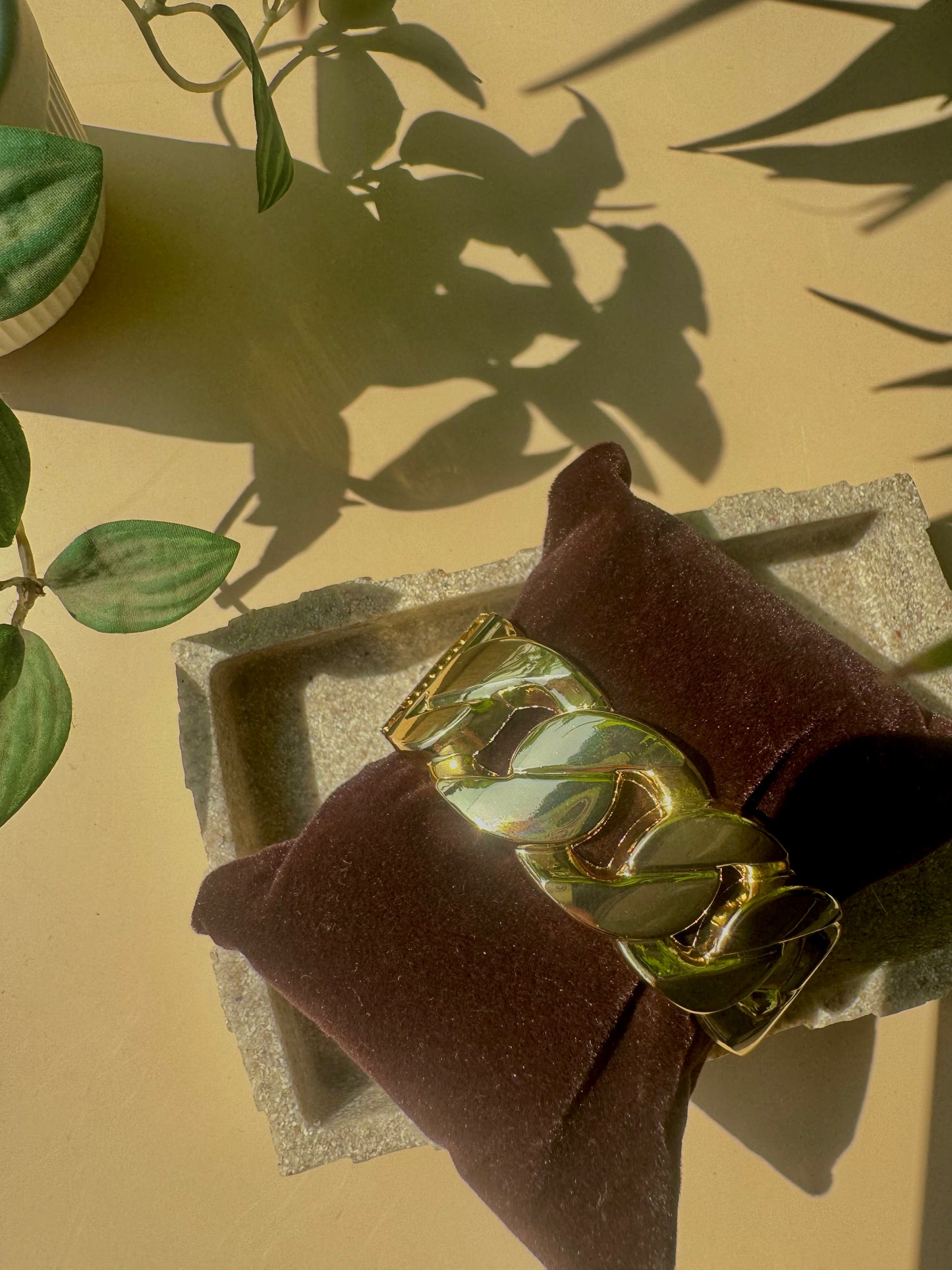 A set of gold-colored jewelry featuring the timeless link design. The set is artfully arranged on a textured tray with subtle green leaves visible in the background.