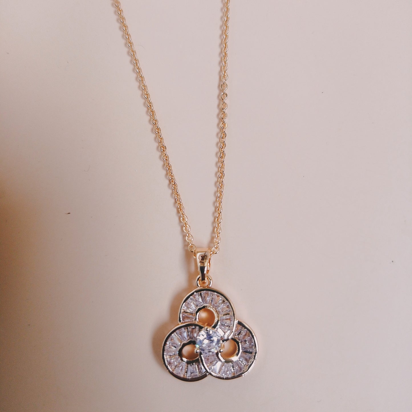 Delicate gold chain necklace with a trio-clover-shaped pendant featuring sparkling gemstones, displayed on a neutral surface