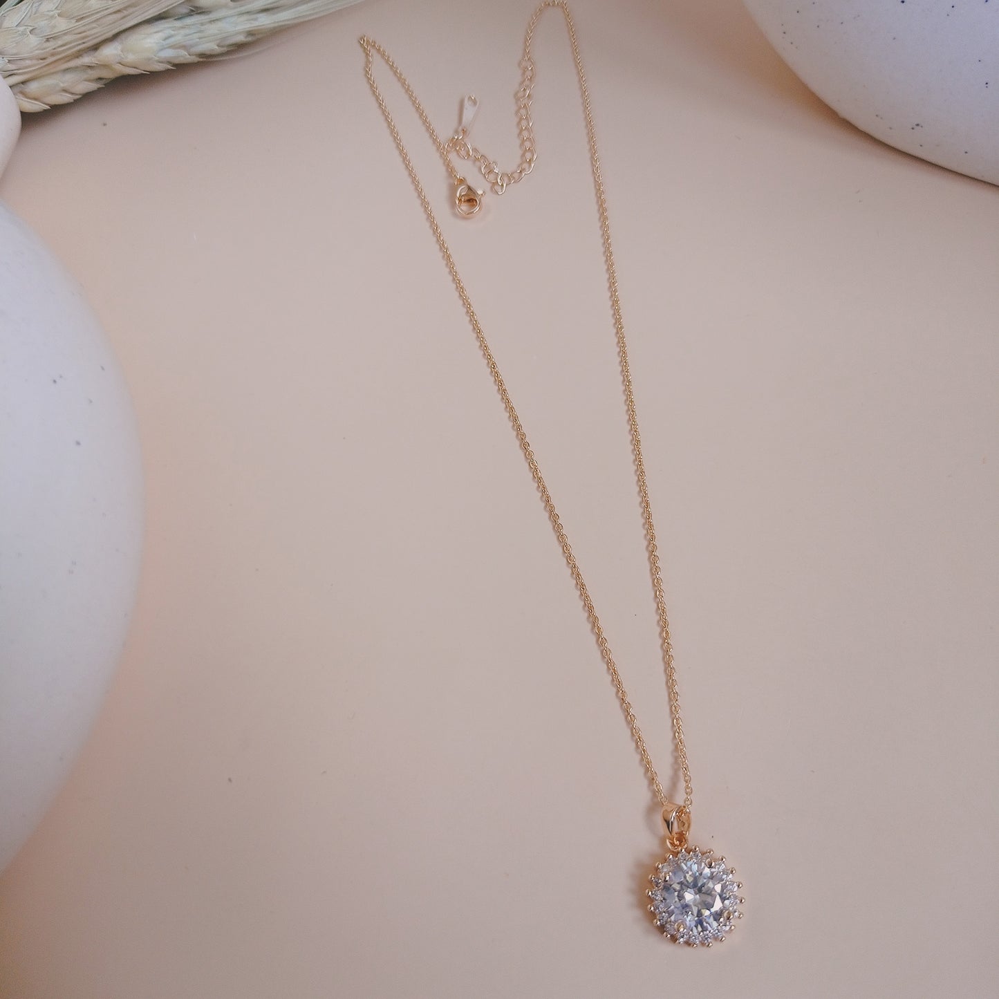 Elegant gold chain necklace featuring a dazzling round-cut blue gemstone pendant, surrounded by a halo of smaller stones, set against a neutral background