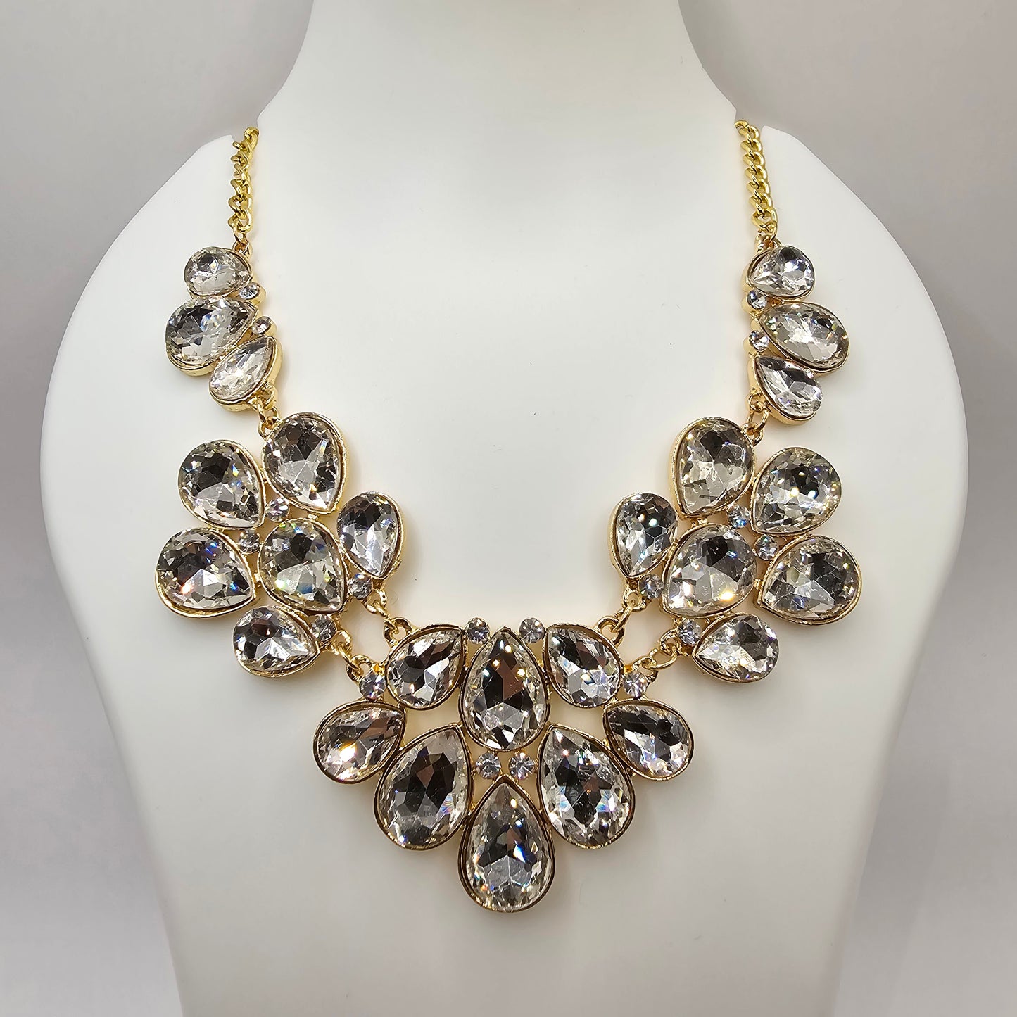 A stunning gold-tone statement necklace featuring an array of clear, faceted teardrop-shaped crystals arranged in a floral-inspired design, elegantly displayed on black satin fabric inside a jewelry box.