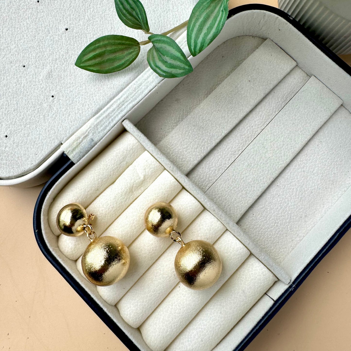 Gold double ball drop earrings in a jewelry case.