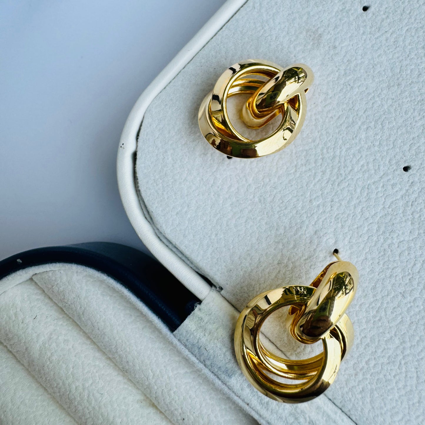 Two polished gold hoop earrings displayed in a cushioned jewelry case