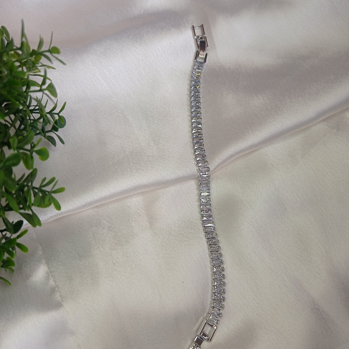 Stunning silver bracelet adorned with sparkling baguette-cut gemstones, elegantly displayed on soft satin fabric with a touch of greenery