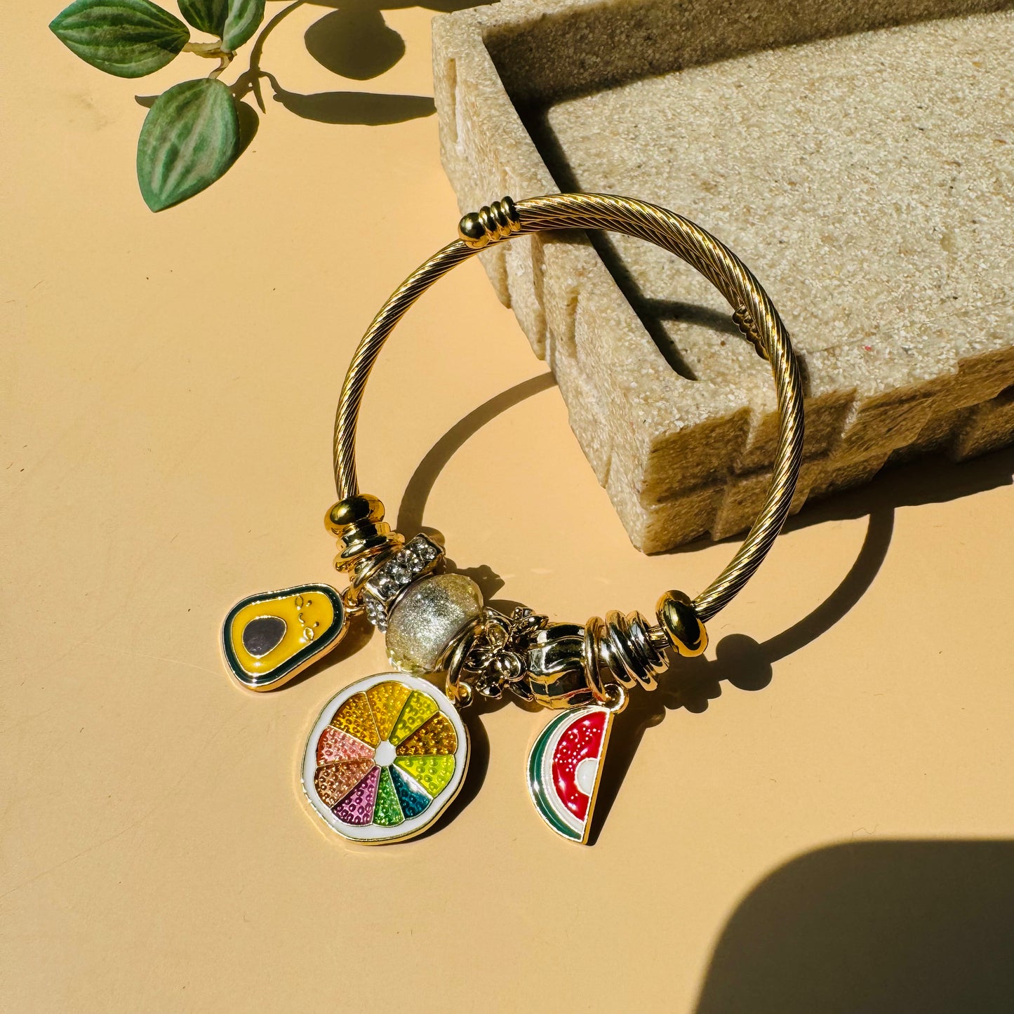 A customizable charm bracelet with a gold-toned base and several unique fruit charms. This style could be found in Mumbai.