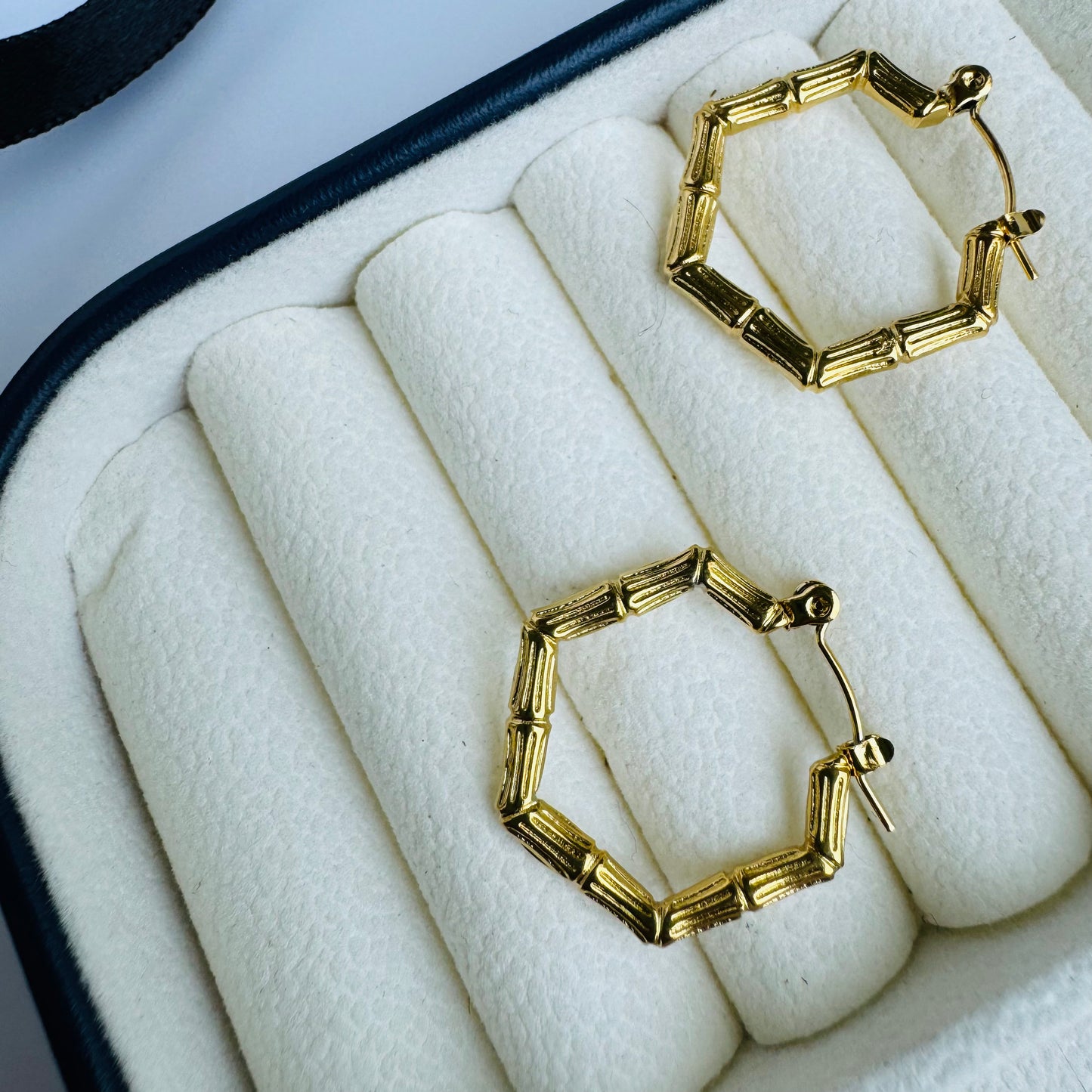 Stylish gold hexagonal hoop earrings displayed in a luxurious cream jewelry case, combining geometric elegance with modern sophistication