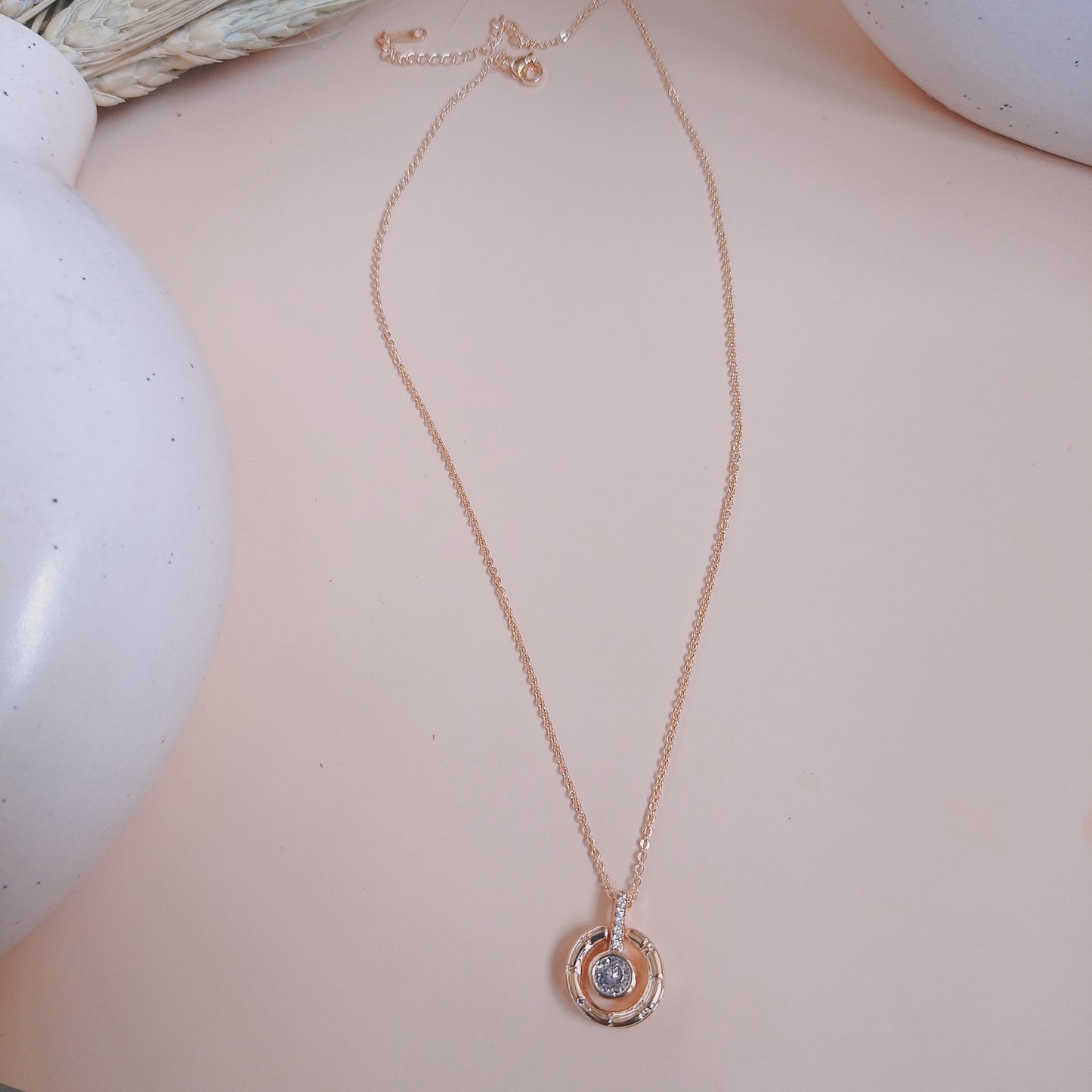Elegant rose gold necklace with a circular pendant featuring a central blue gemstone, accented with sparkling white stones on the bail, set against a neutral background