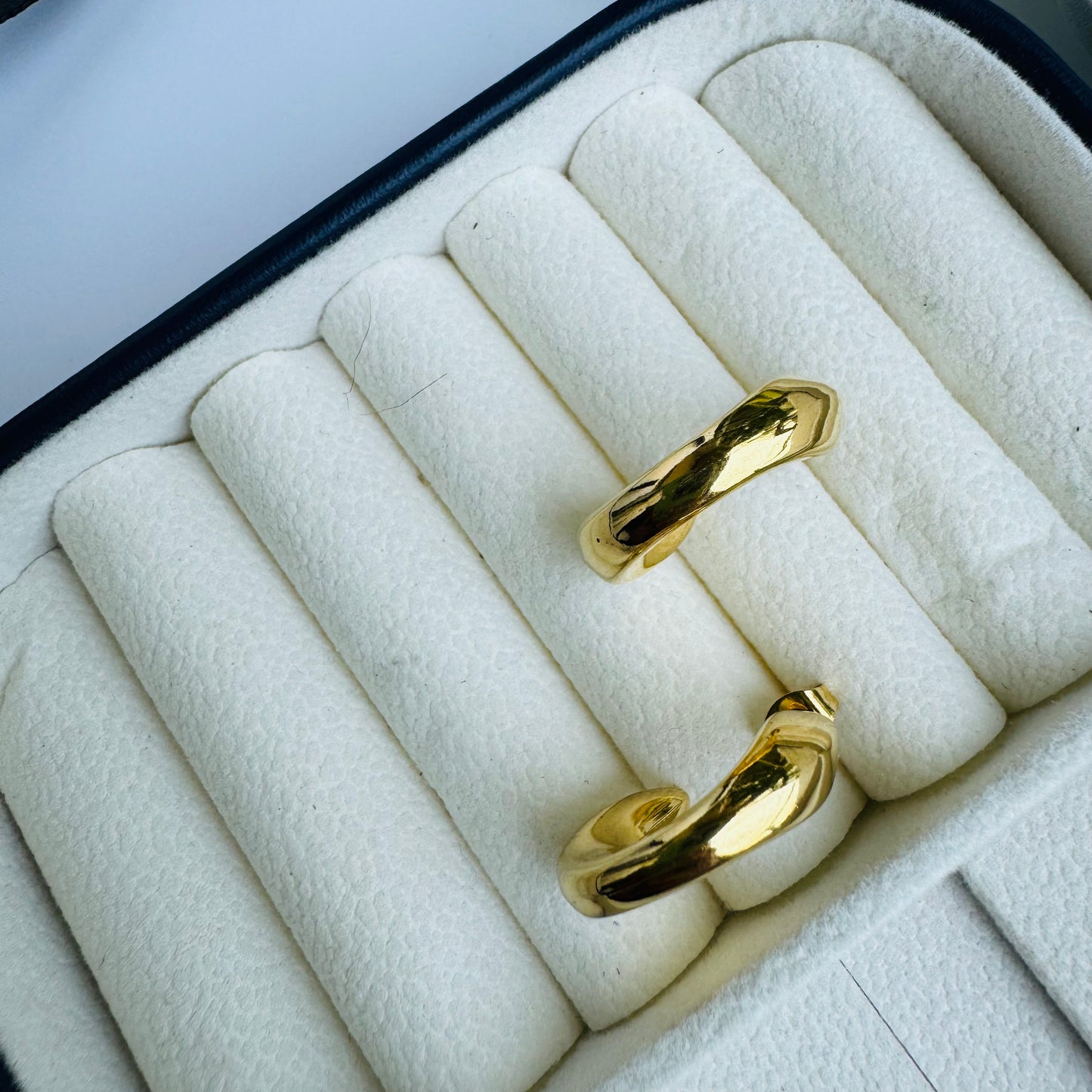 The earrings are circular or semi-circular in shape and appear to be made of a shiny, yellow metal, consistent with the appearance of gold. They are displayed in a jewelry case, suggesting they are a valuable item