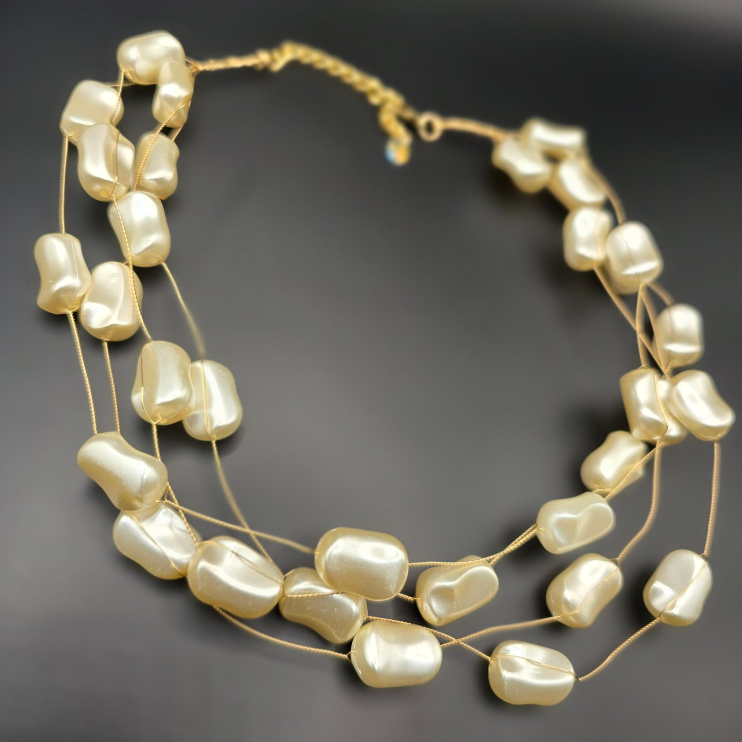 A delicate multi-strand necklace featuring irregular-shaped ivory pearls on fine gold wires, elegantly displayed on a black velvet bust.