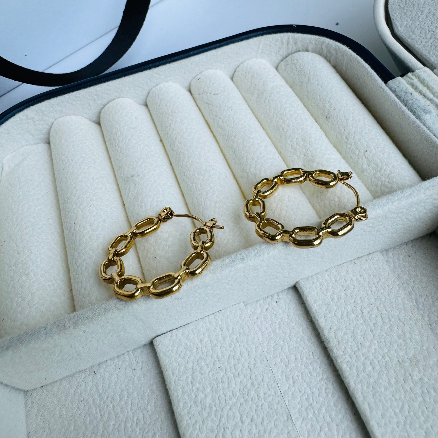 Elegant gold chain-link hoop earrings displayed in a plush, cream-colored jewelry case, exuding sophistication and contemporary charm.