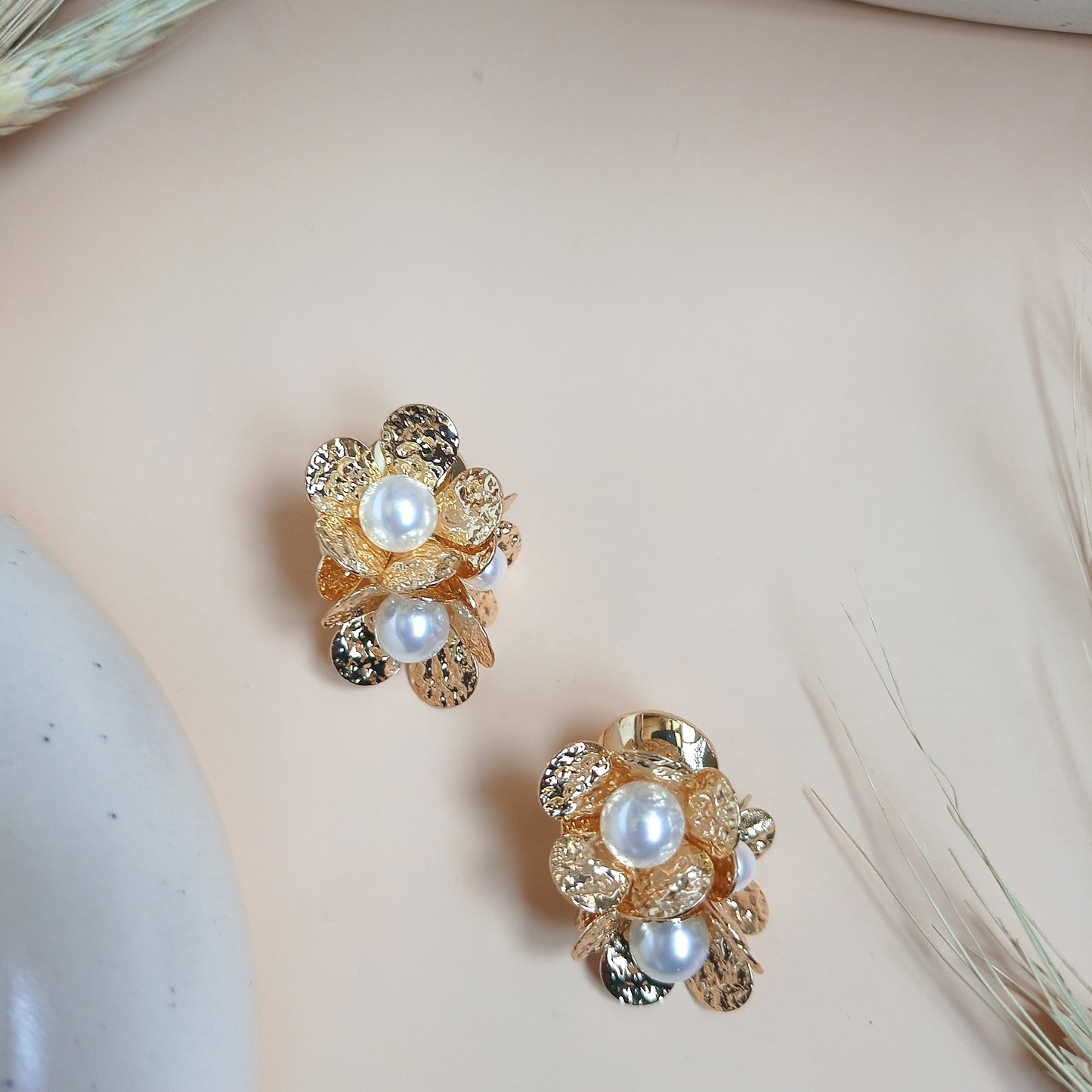 This pair of earrings features an intricate gold-tone floral design with multiple layers of textured petals, accented by luminous pearls at the center and edges. A perfect blend of elegance and modern sophistication, these statement earrings add a refined touch to any outfit.