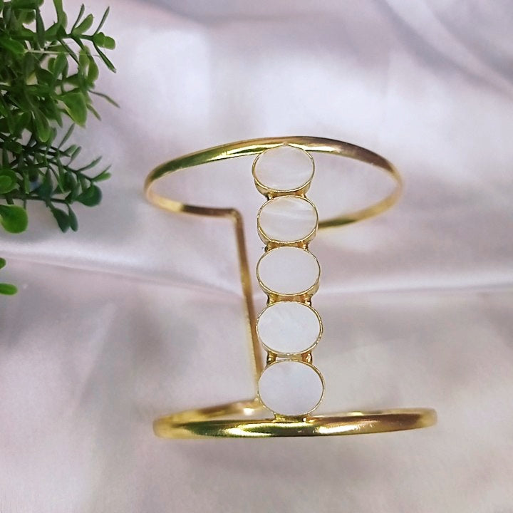 Elegant gold cuff bracelet with white circular accents, worn by a woman in a stylish mauve outfit, complementing her chic and minimalistic look.