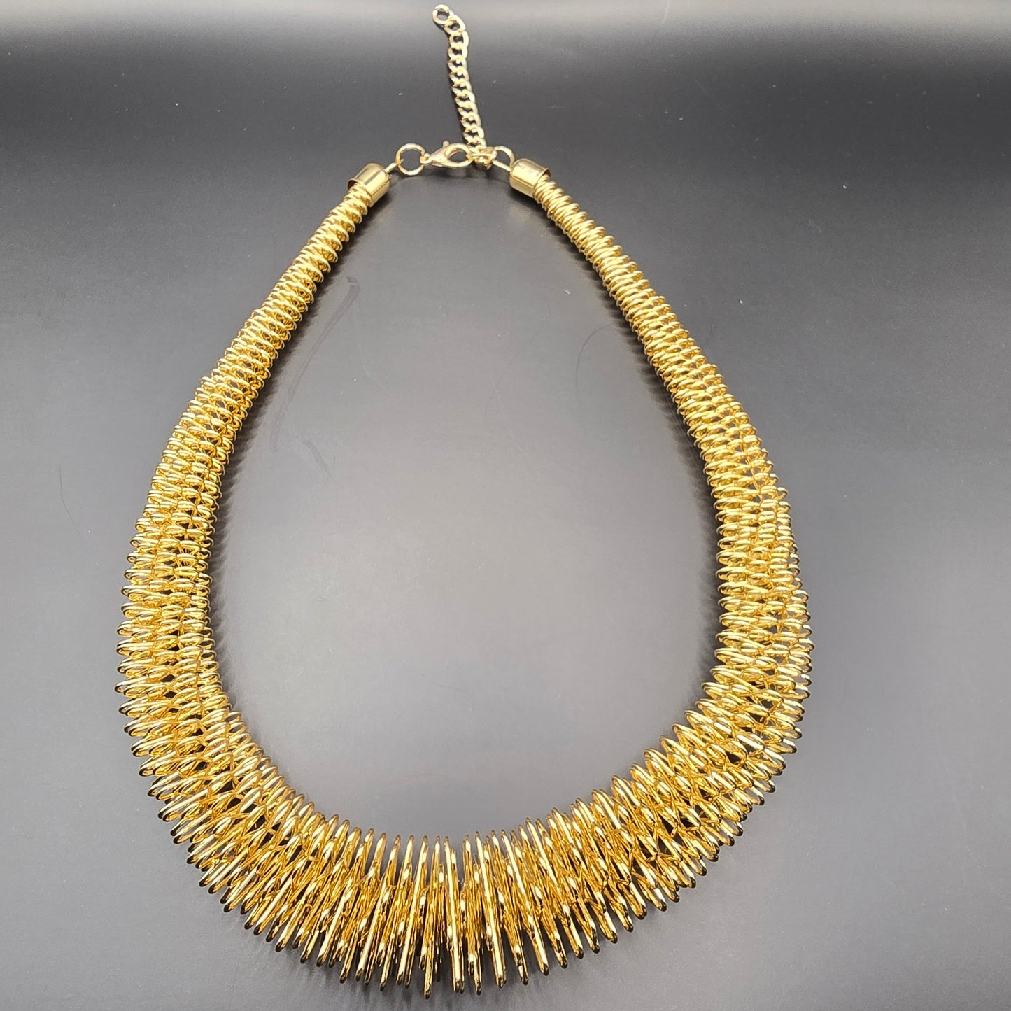 A bold, adjustable gold choker necklace with a spiky, collar-like design is presented on a white display. Lush 24 branded packaging suggests it is a high-fashion item