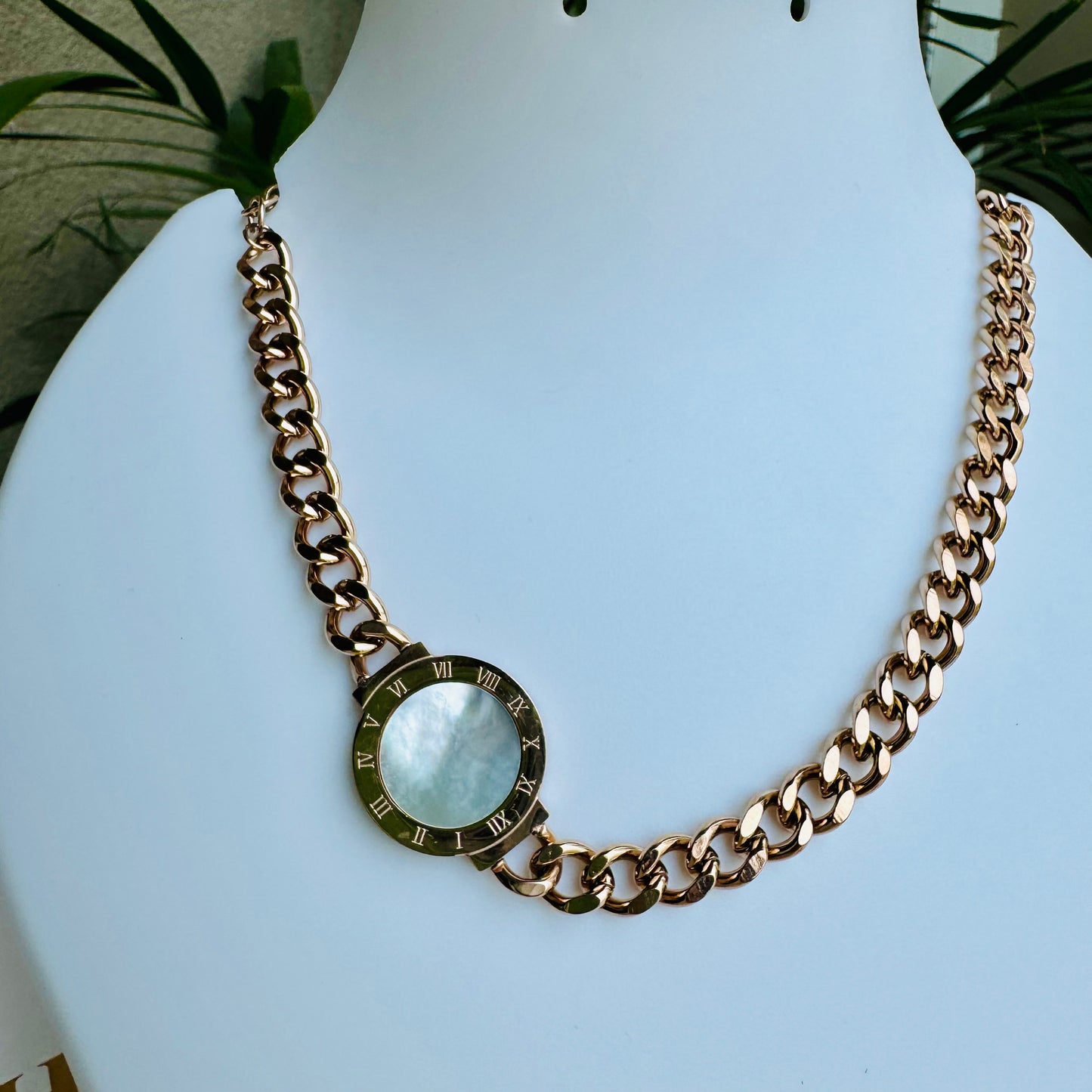 Elegant gold chain necklace with a chunky curb-link design, featuring a single circular pendant with a faceted crystal accent. The minimalist yet bold style makes it a versatile statement piece. Displayed on a white mannequin with luxury packaging in the background.