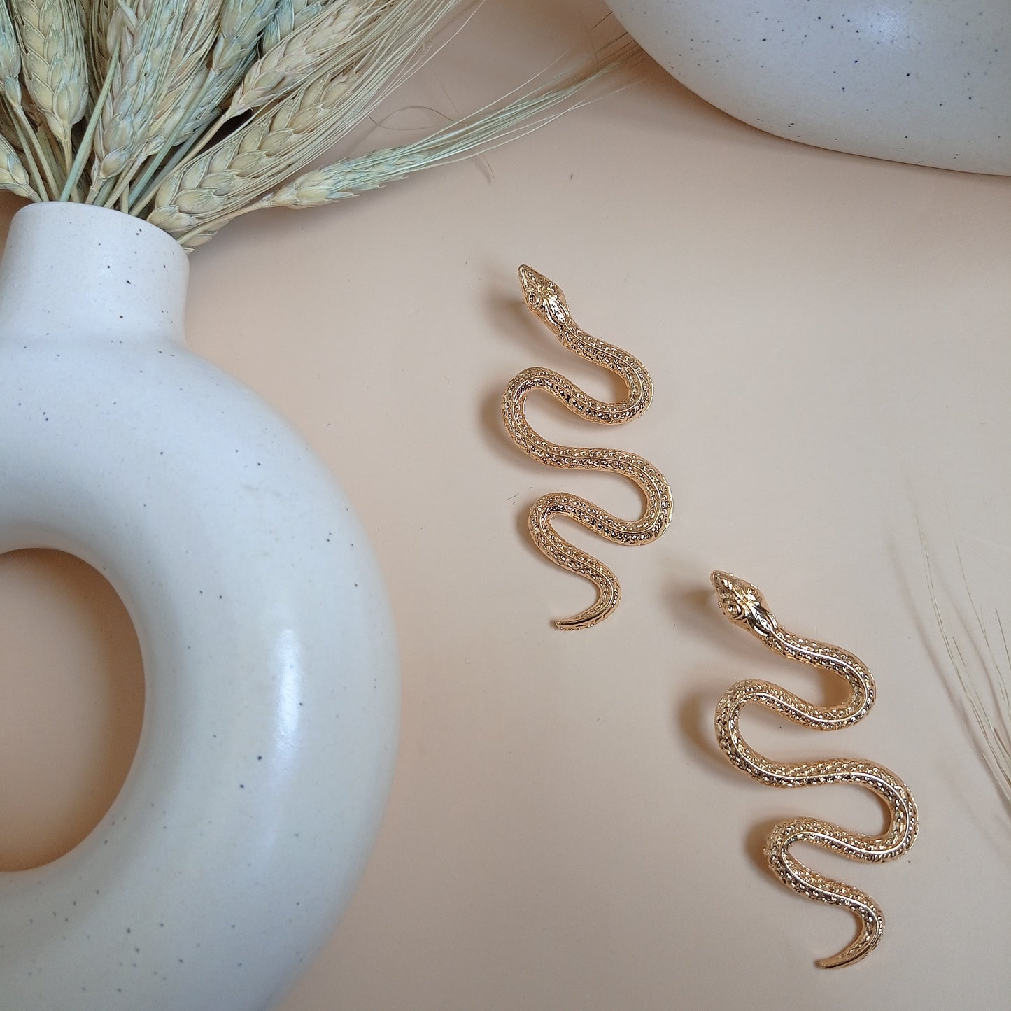 Elegant gold snake earrings with intricate detailing, draped over a modern ceramic vase, creating a bold and stylish statement accessory