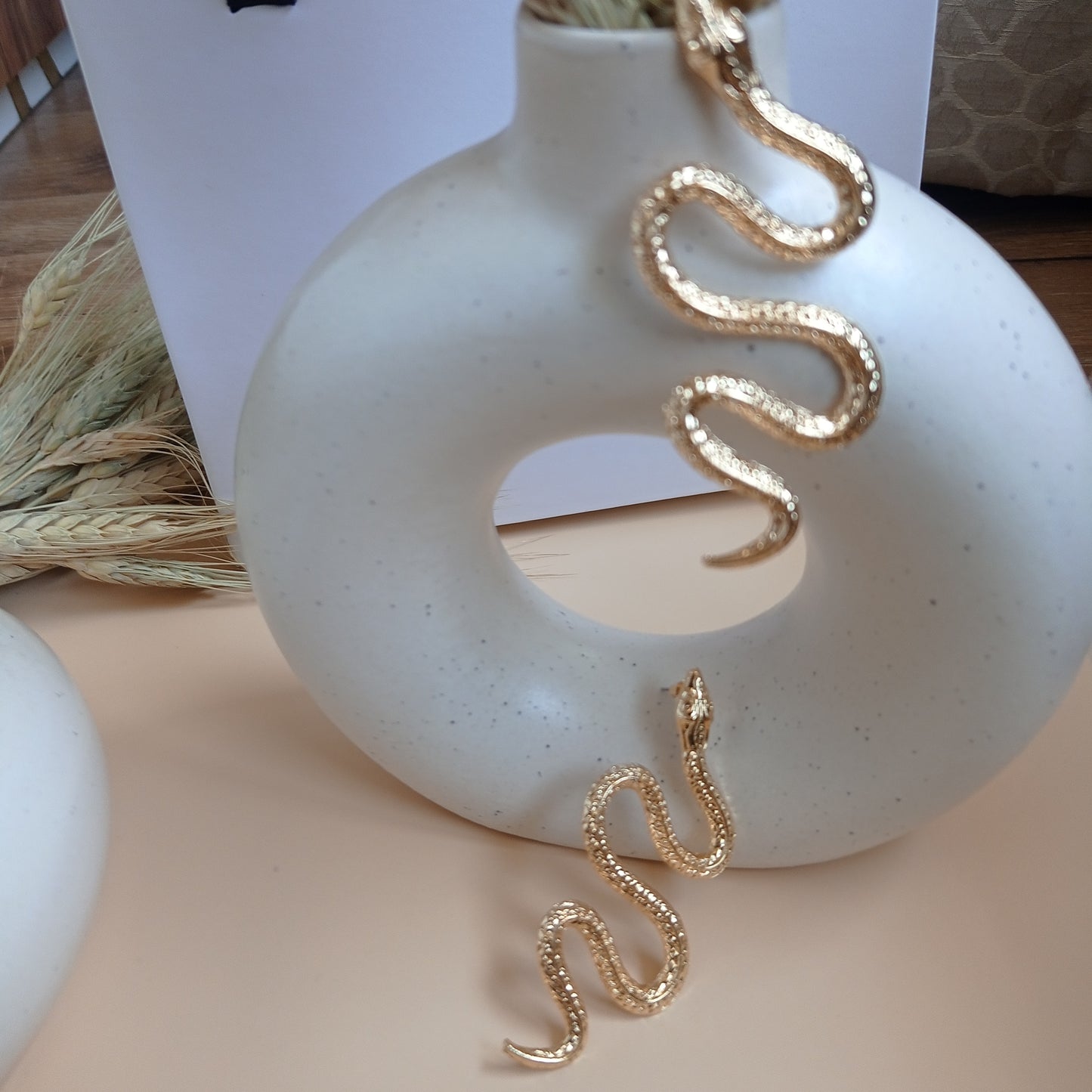 Elegant gold snake earrings with intricate detailing, draped over a modern ceramic vase, creating a bold and stylish statement accessory