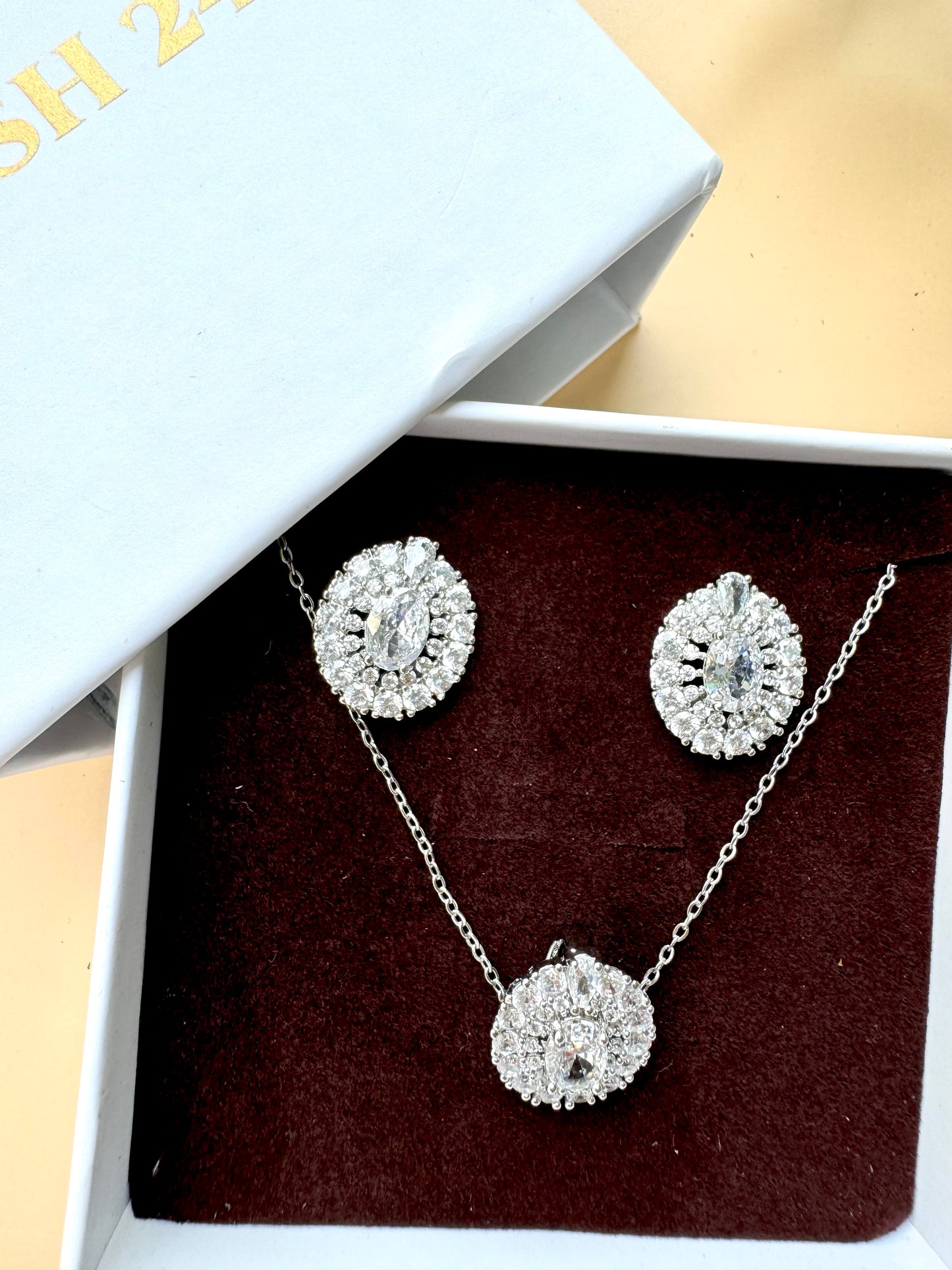 A set of sparkling silver-toned jewelry featuring flower-shaped designs with clear crystals. The set includes a pendant necklace and matching stud earrings, presented in a light blue LUSH 24 branded gift box with a black velvet insert.