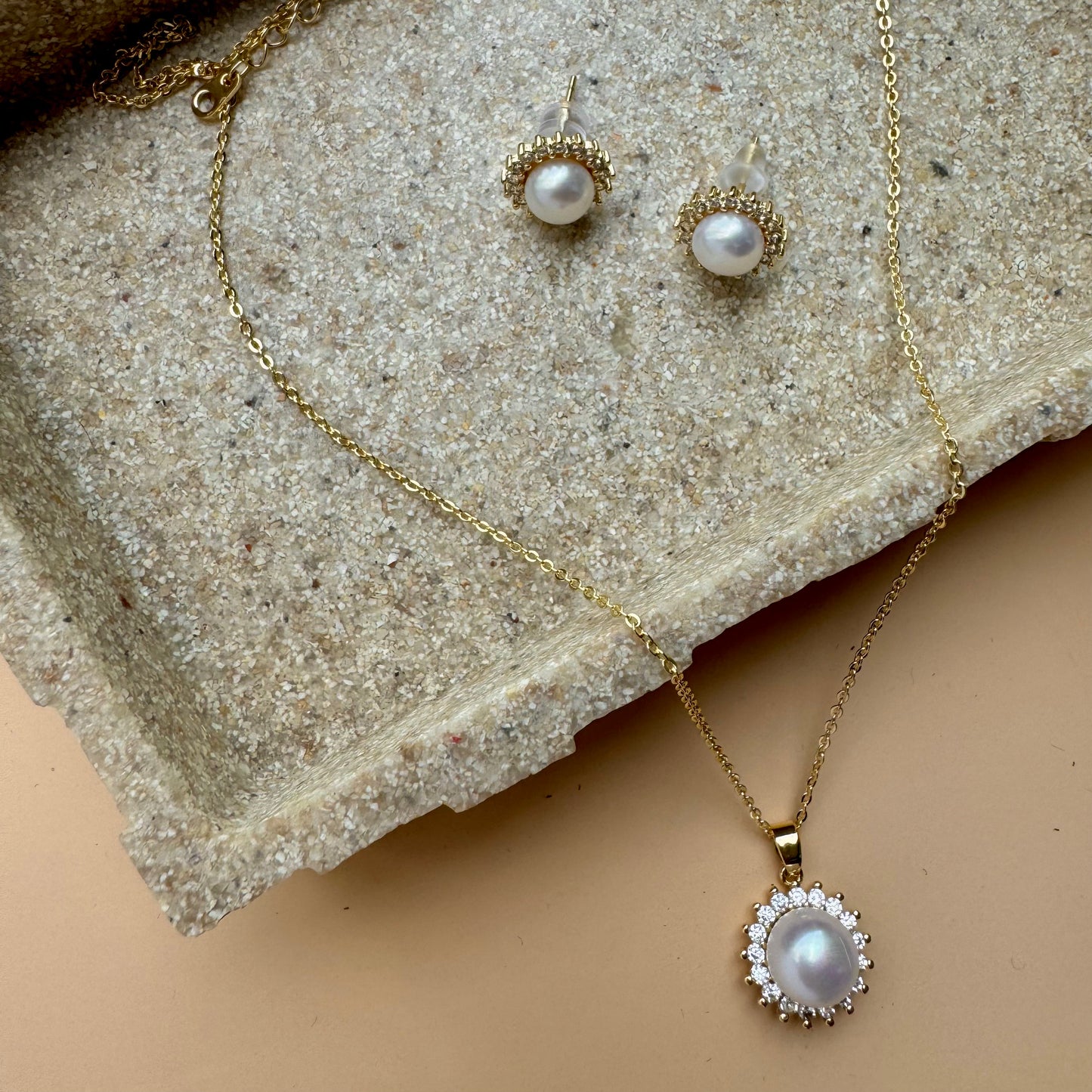 A timeless jewelry set featuring a natural freshwater pearl pendant necklace with a gold setting and a halo of sparkling clear stones. Matching pearl stud earrings with the same halo design complete the set, likely available in Mumbai, Maharashtra, India.