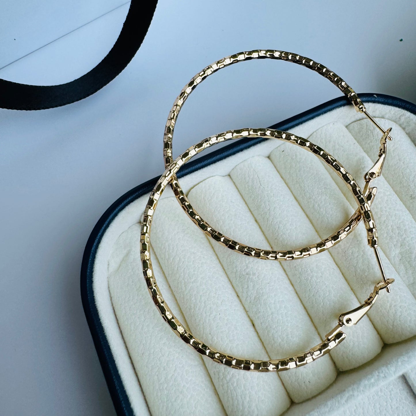 Elegant textured gold hoop earrings displayed in a luxurious jewelry case, showcasing their classic yet modern appea