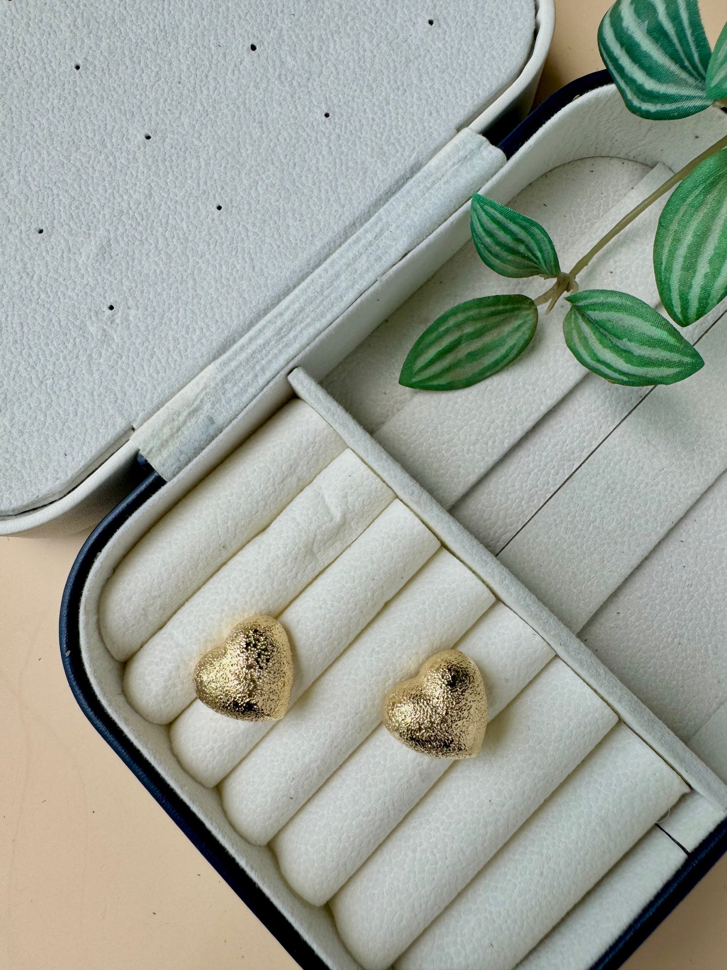 An 18k gold-plated stainless steel earrings designed to be tarnish-free and waterproof, displayed on a small brown cushion.