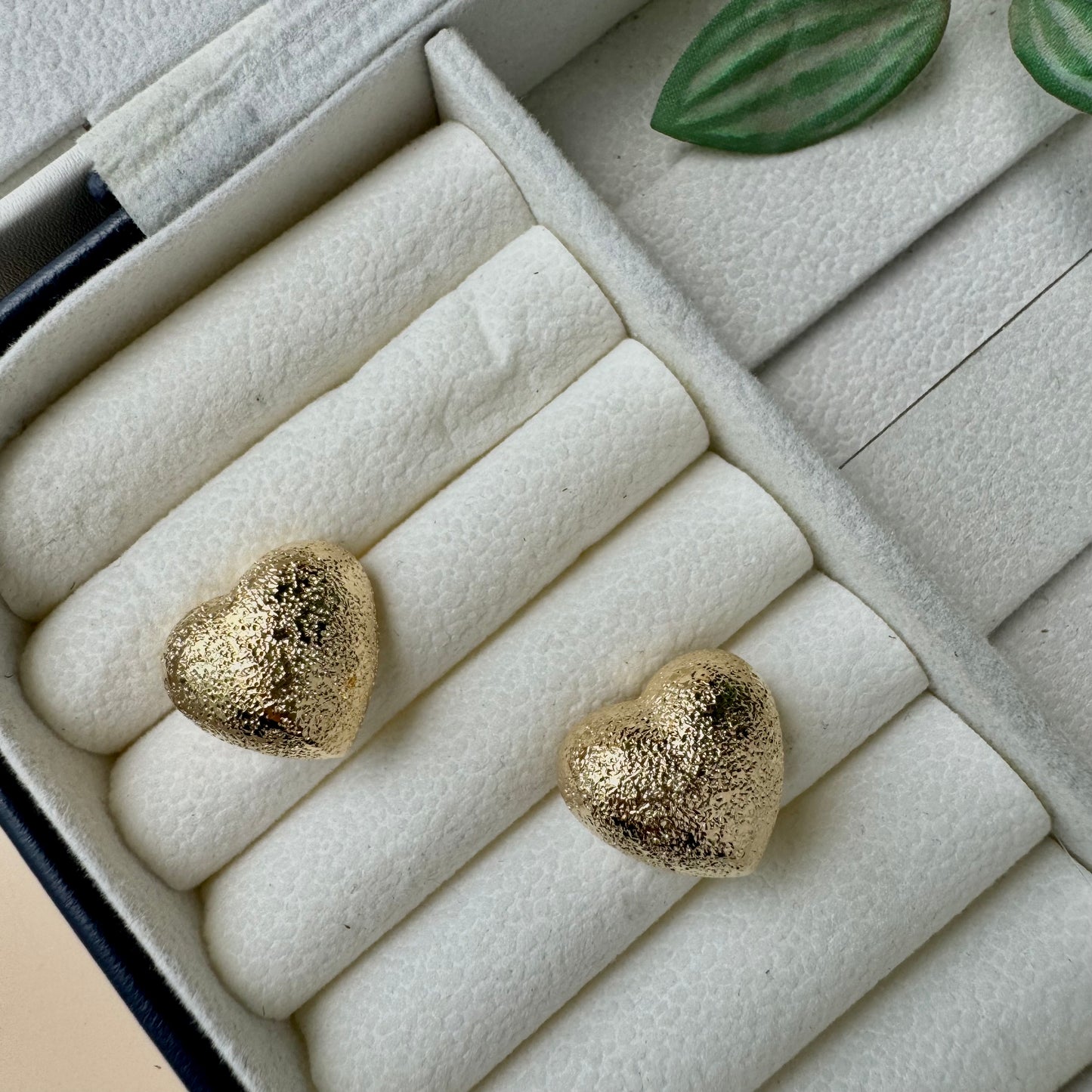 An 18k gold-plated stainless steel earrings designed to be tarnish-free and waterproof, displayed on a small brown cushion.