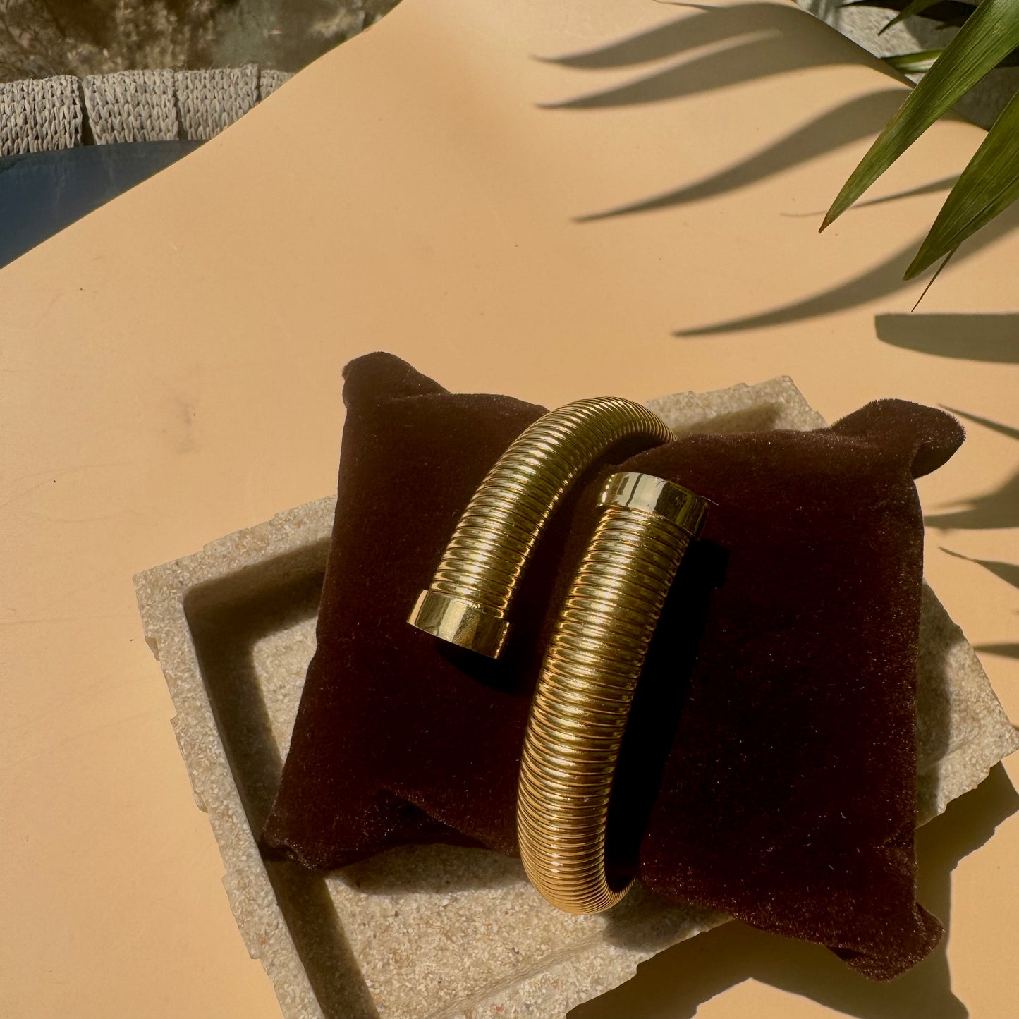 Gold ribbed cuff bracelet on a brown cushion