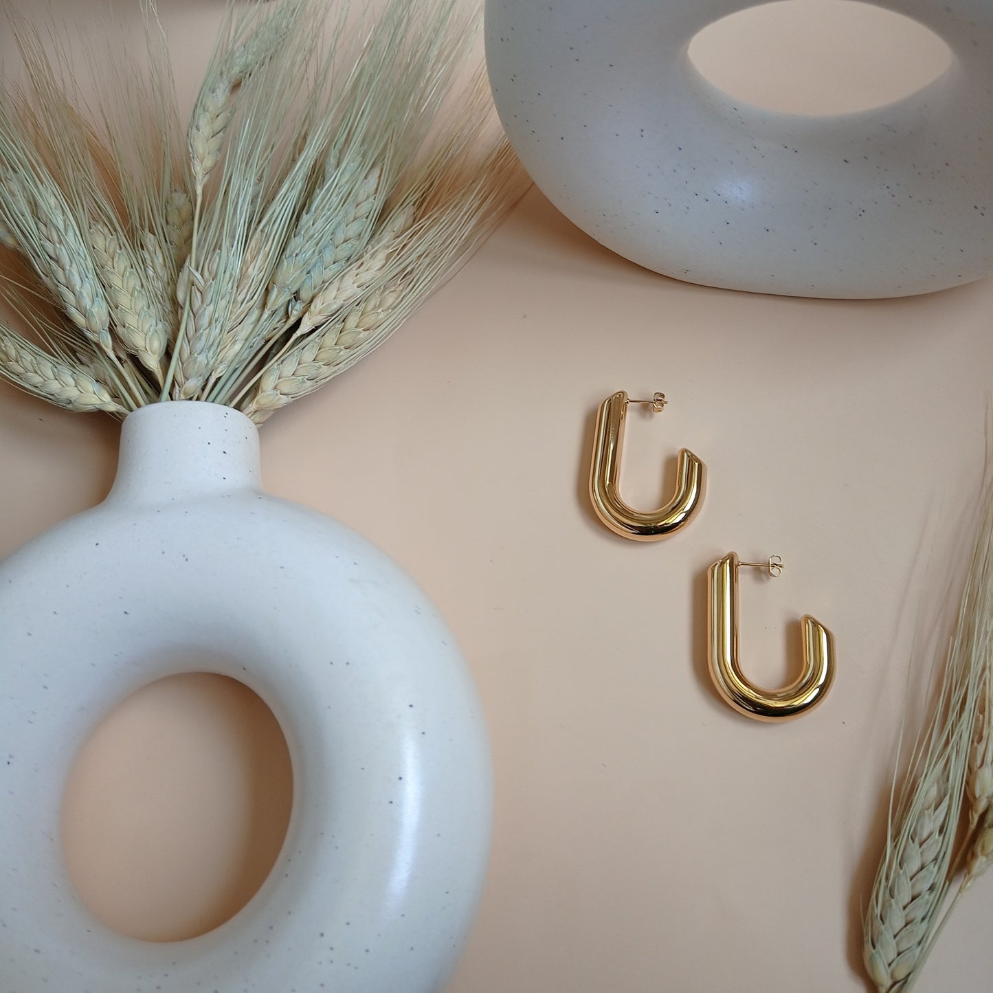 Minimalist gold U-shaped hoop earrings, exuding modern elegance, set against a neutral-toned backdrop with ceramic accents