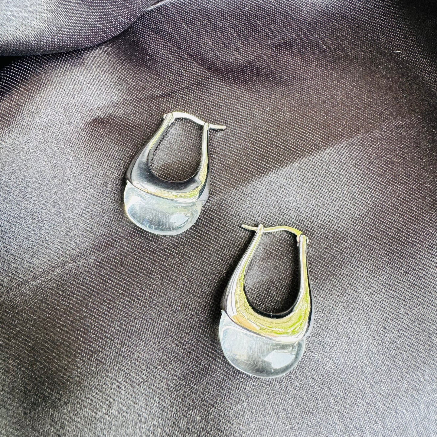 Sleek and modern silver earrings with a fluid, organic design, elegantly displayed on black satin in a premium gift box