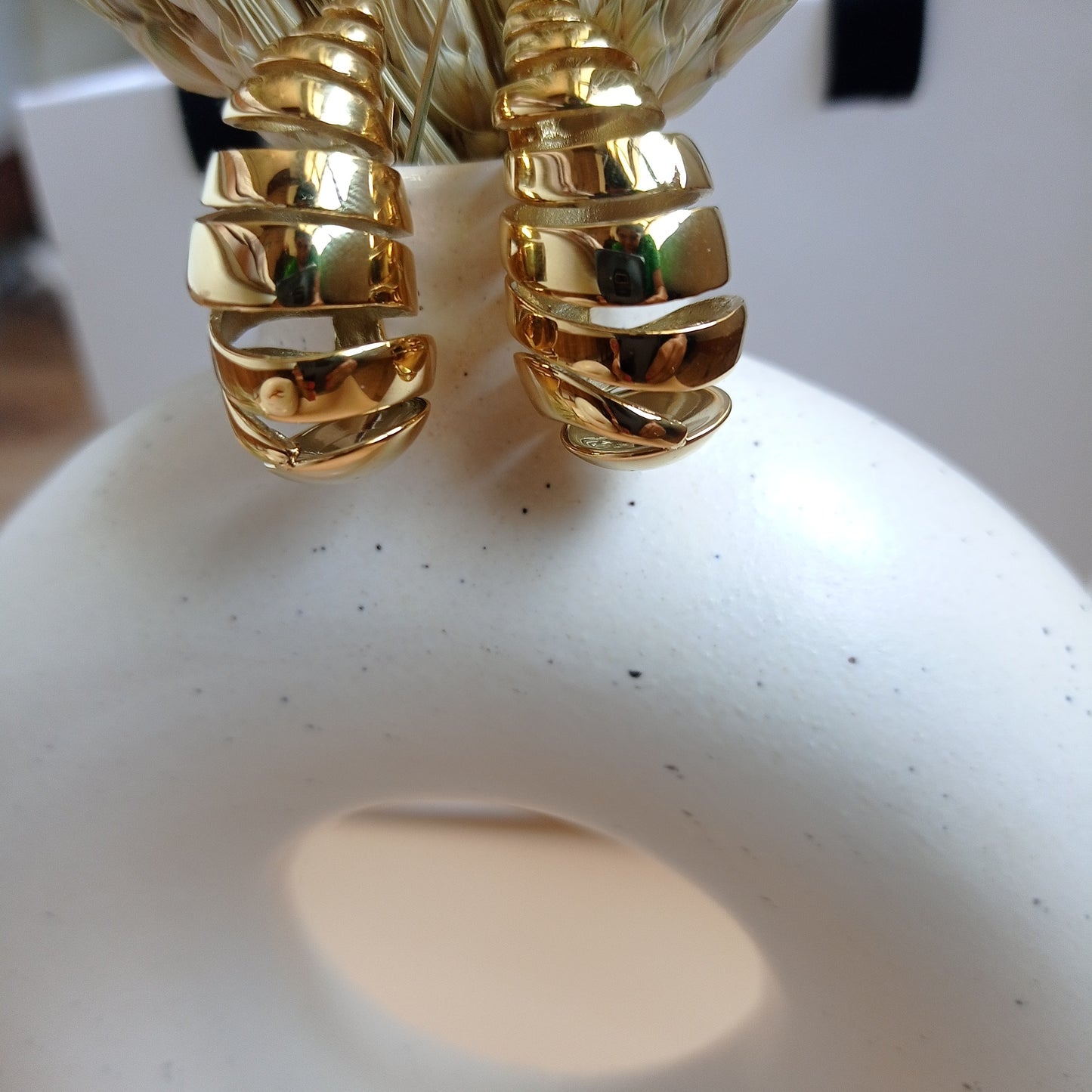 Bold gold statement earrings with a modern, layered design, elegantly displayed on a minimalist ceramic vase for a sophisticated look.