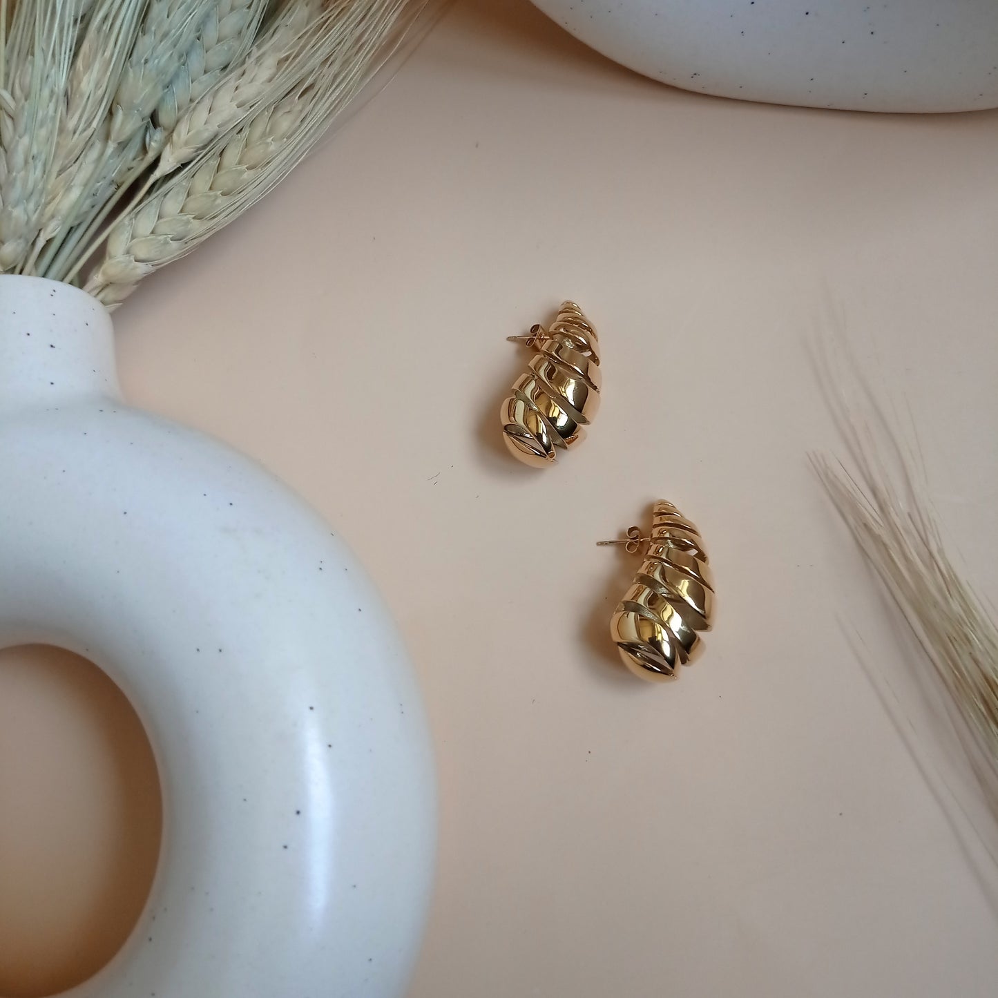 Bold gold statement earrings with a modern, layered design, elegantly displayed on a minimalist ceramic vase for a sophisticated look.