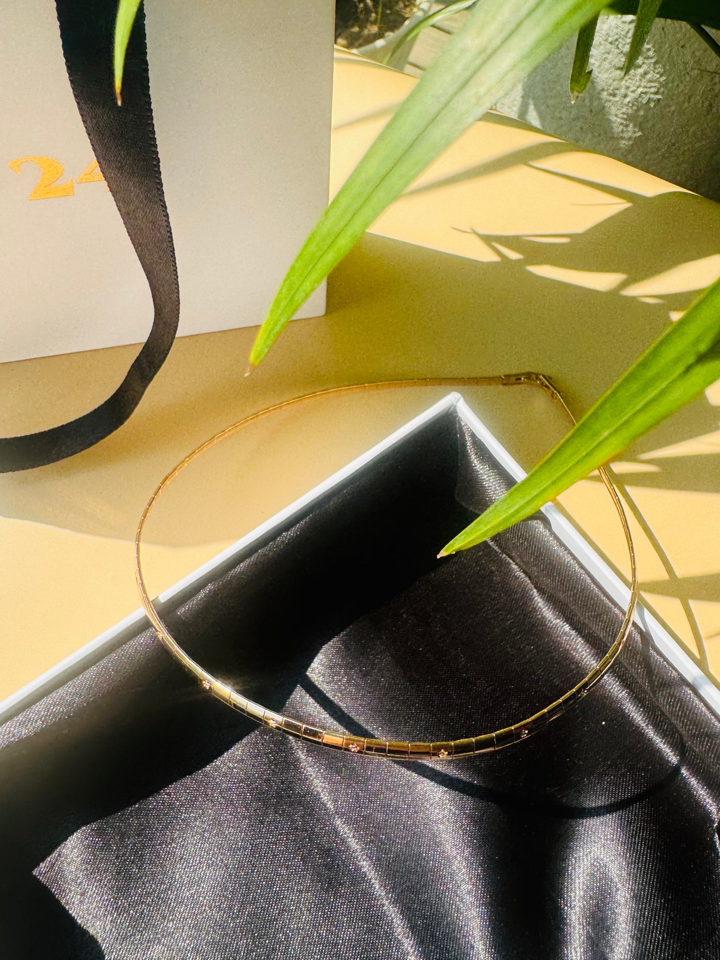 Close-up of a ultra luxe thin necklace with delicate chains in gold finishes, connected by a single clasp. It is nestled in a Lush 24 branded gift box