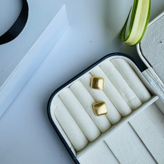 Two delicate square studs earrings displayed in a cushioned jewelry case