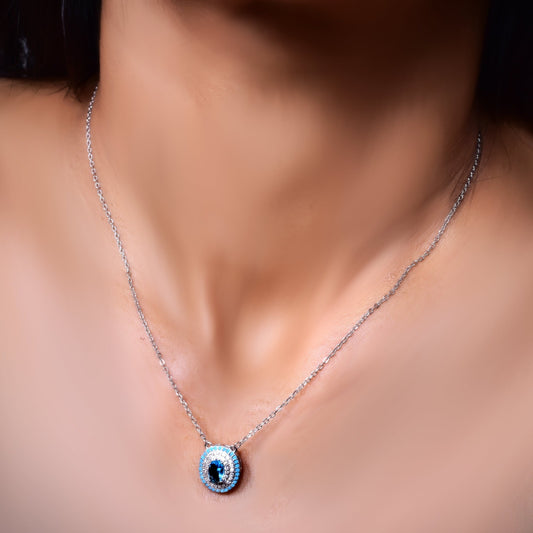 Stylish silver necklace featuring an evil eye pendant encrusted with blue and white crystals, elegantly worn for a protective and fashionable look