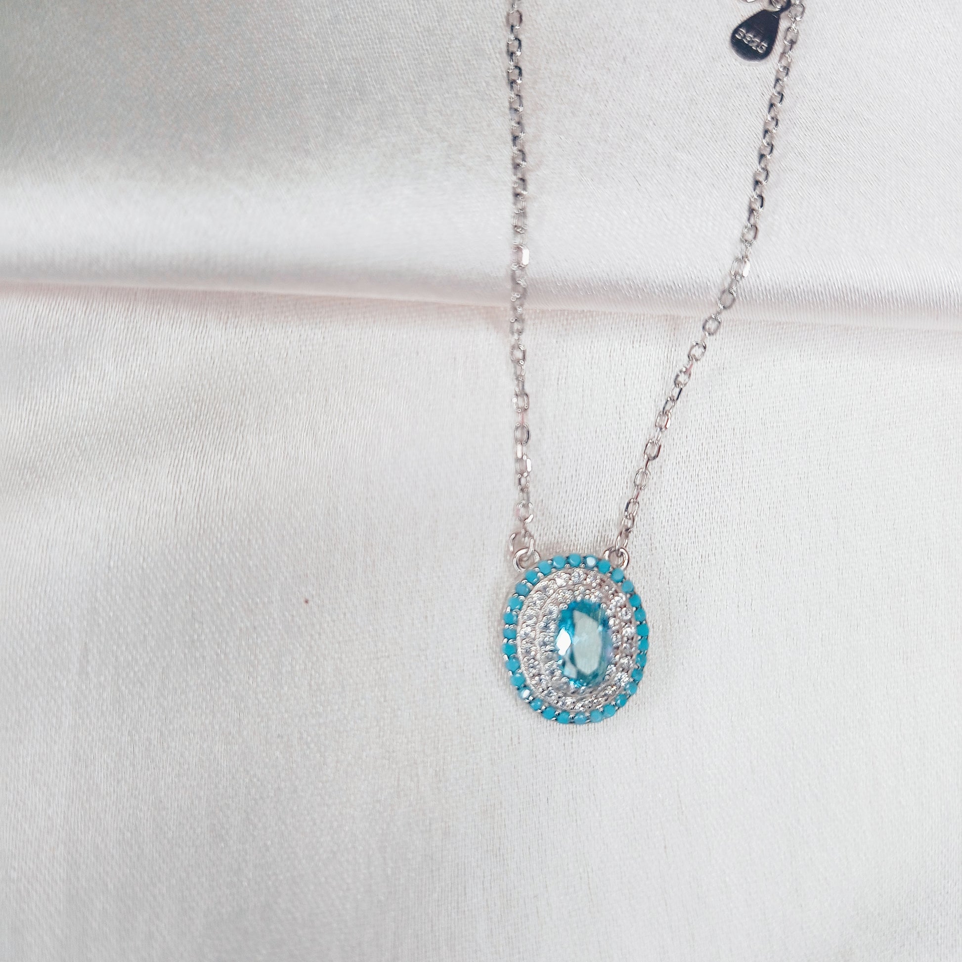 Stylish silver necklace featuring an evil eye pendant encrusted with blue and white crystals, elegantly worn for a protective and fashionable look