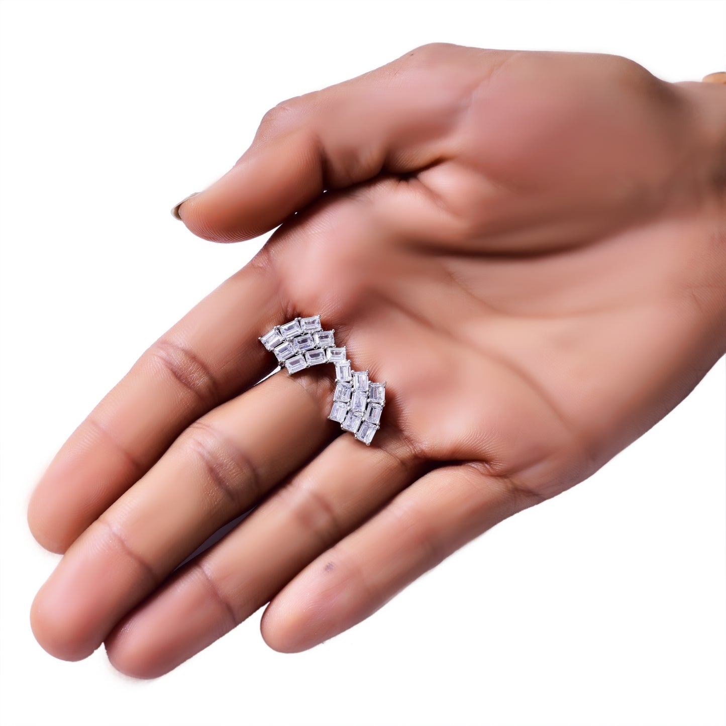 Close-up of a hand holding a pair of elegant silver-tone ear climbers adorned with a row of sparkling baguette-cut stones arranged in a curved, geometric pattern. These statement earrings add a modern yet sophisticated touch to any look