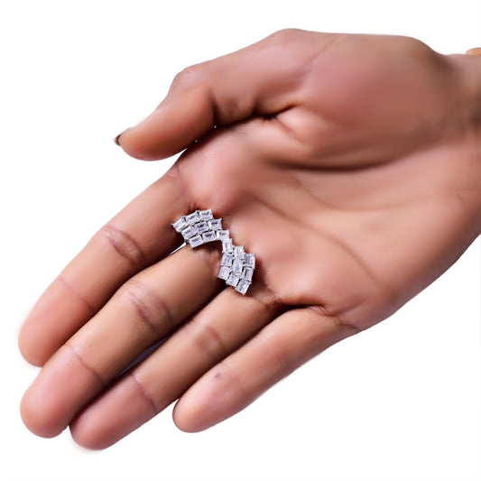 Close-up of a hand holding a pair of elegant silver-tone ear climbers adorned with a row of sparkling baguette-cut stones arranged in a curved, geometric pattern. These statement earrings add a modern yet sophisticated touch to any look