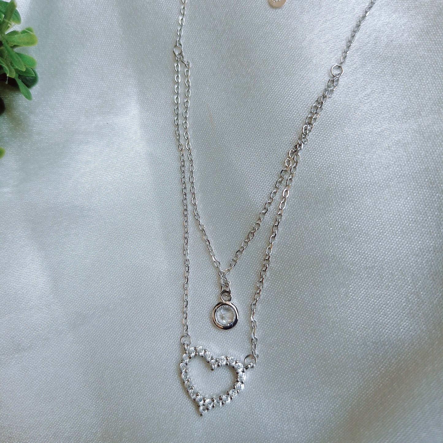 Elegant layered silver necklace featuring a delicate solitaire pendant on the upper chain and a sparkling crystal-studded heart pendant on the lower chain, adding a touch of sophistication and charm