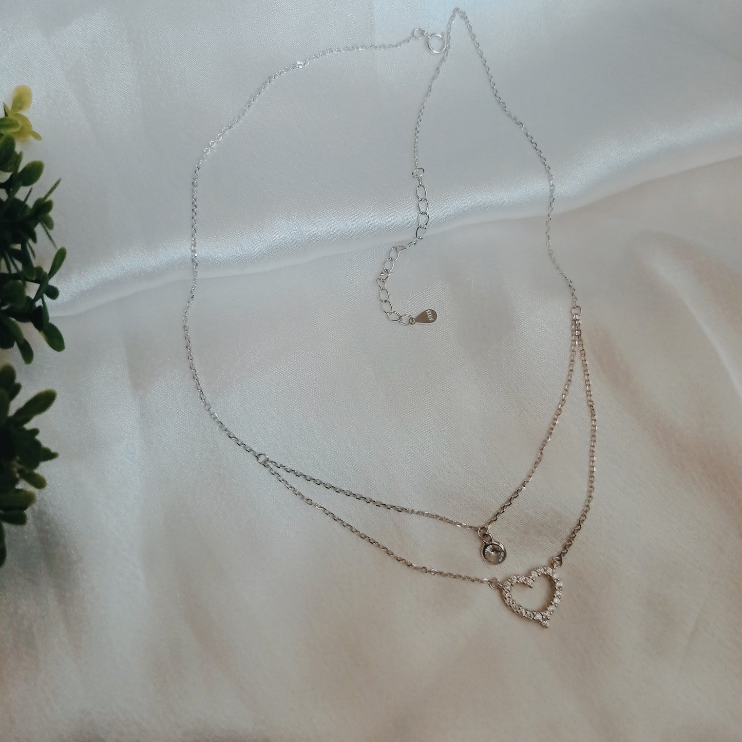 Elegant layered silver necklace featuring a delicate solitaire pendant on the upper chain and a sparkling crystal-studded heart pendant on the lower chain, adding a touch of sophistication and charm