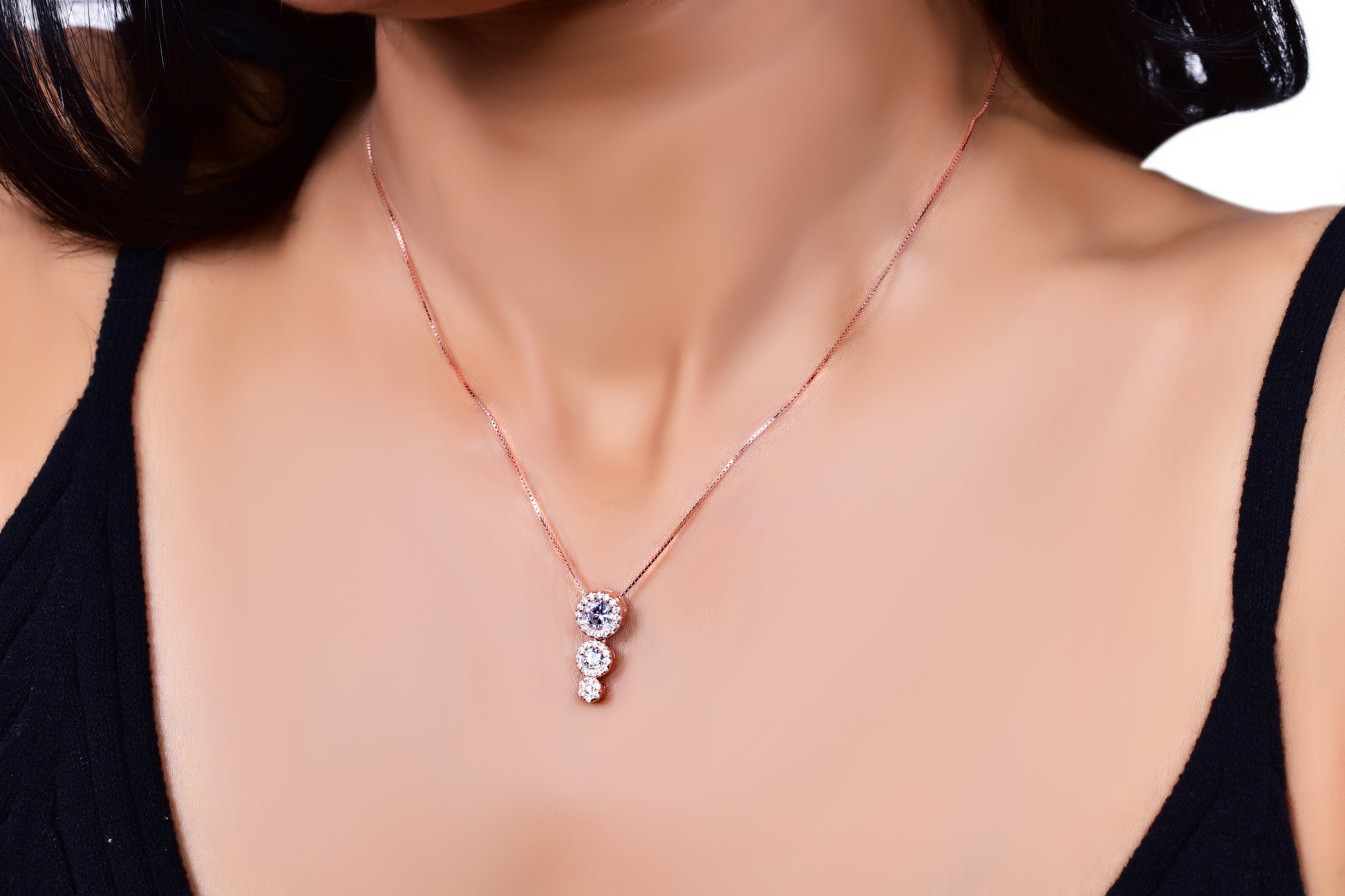 Elegant rose gold necklace featuring a three-stone drop pendant adorned with sparkling crystals, gracefully worn with a black outfit for a sophisticated look