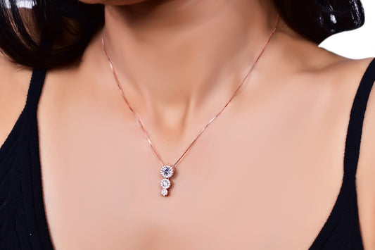Elegant rose gold necklace featuring a three-stone drop pendant adorned with sparkling crystals, gracefully worn with a black outfit for a sophisticated look