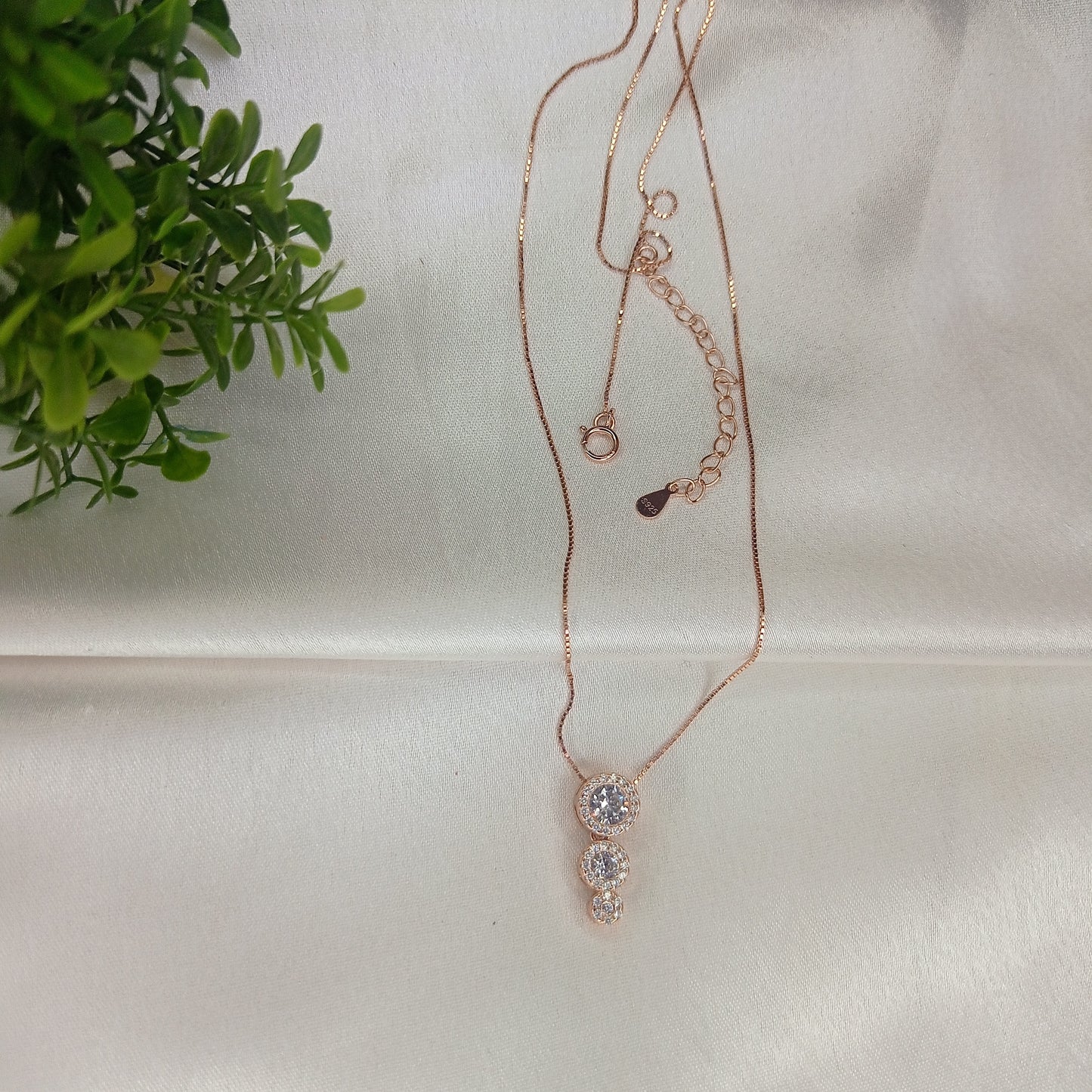 Elegant rose gold necklace featuring a three-stone drop pendant adorned with sparkling crystals, gracefully worn with a black outfit for a sophisticated look