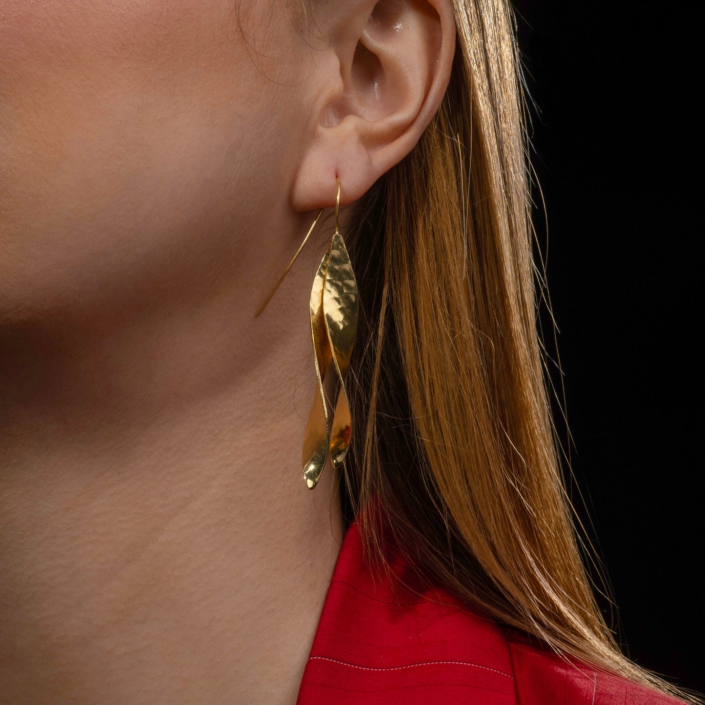 model wearing elegant gold dangle earrings with twisted leaf-like design, featuring a hammered texture for a sophisticated and modern jewelry look