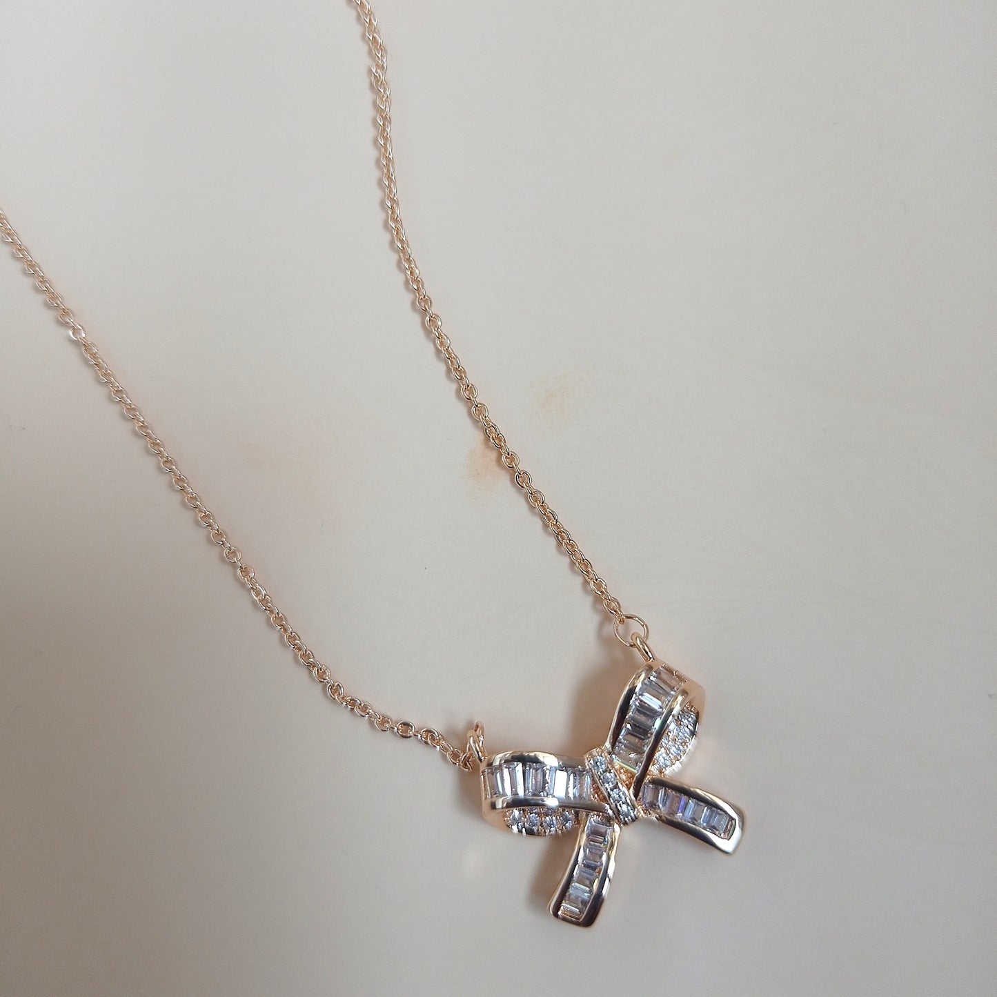 Rose gold necklace with a bow-shaped pendant featuring baguette-cut and round sparkling stones, displayed against a neutral background