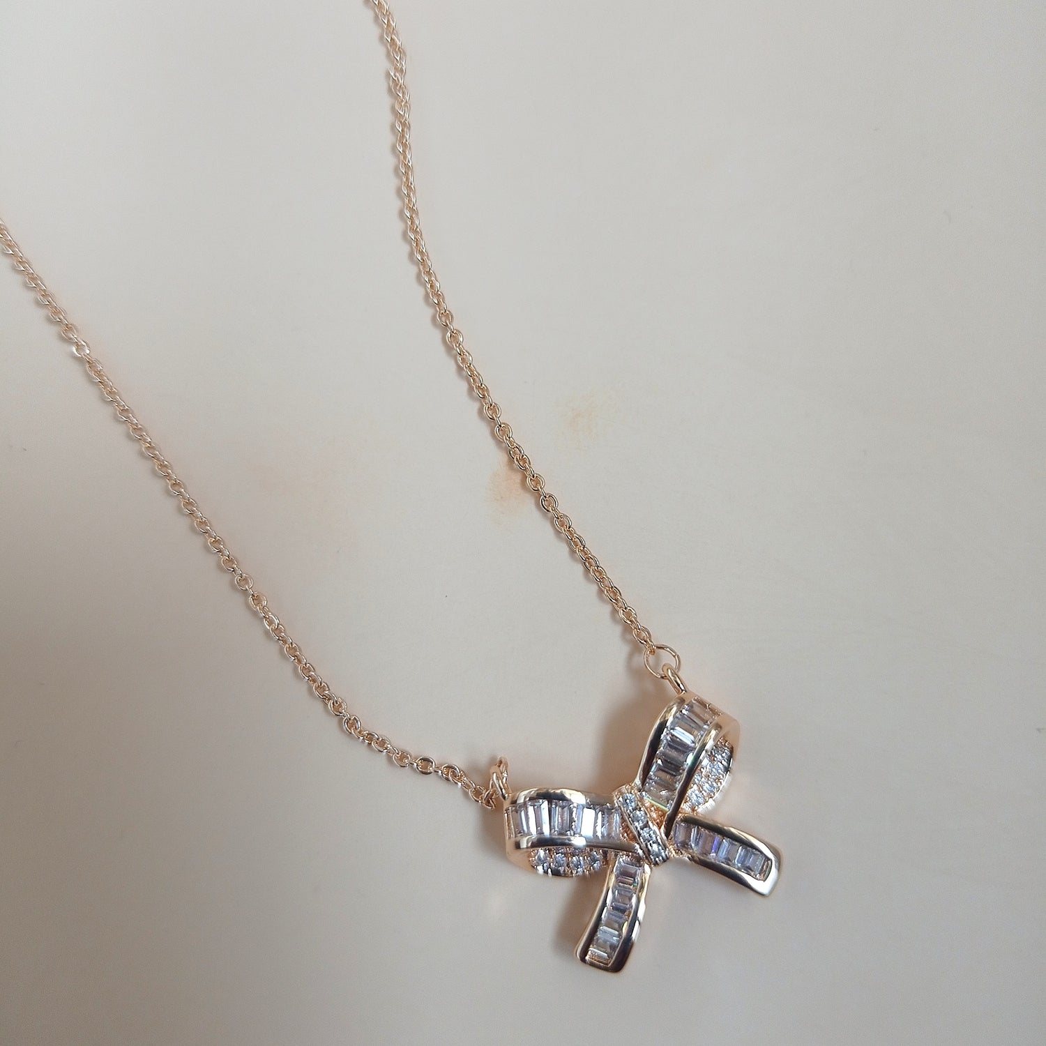 Rose gold necklace with a bow-shaped pendant featuring baguette-cut and round sparkling stones, displayed against a neutral background